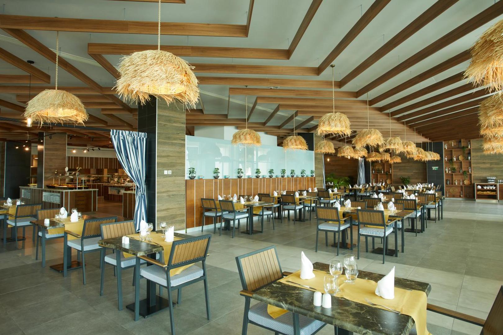 Secrets Sunny Beach Resort and Spa bufetes tipa restorāns ar unikāliem salmu gaismekļiem un plašu sēdvietu zonu piekrastē