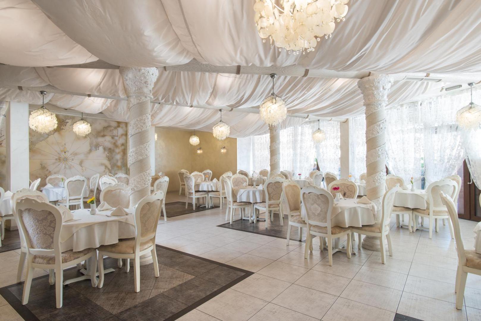 Diamant Residence Hotel & Spa gaišā brokastu zāle ar dekoratīviem griestu audumiem, kolonnām un apaļām lustrām