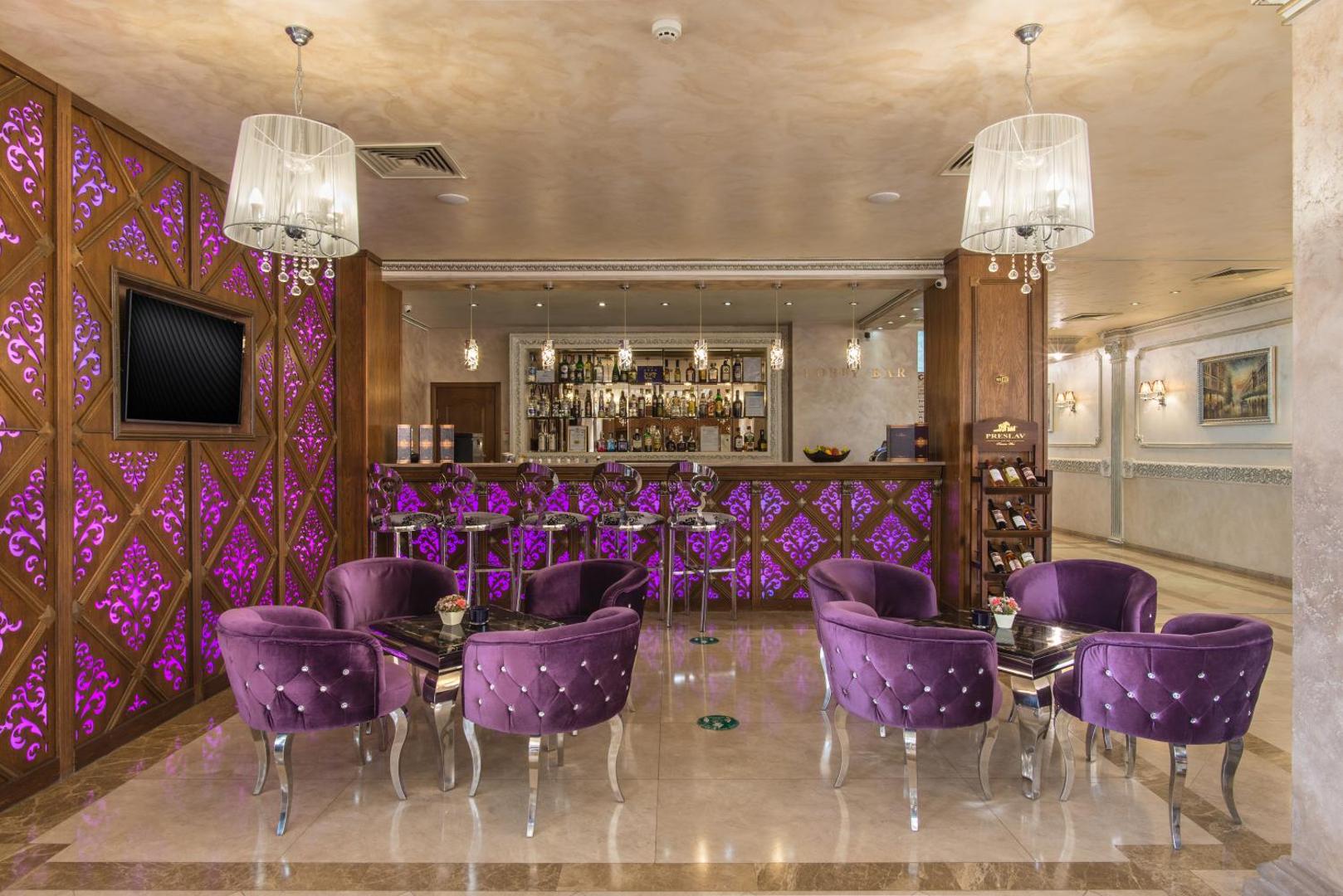 Diamant Residence Hotel & Spa lobby bārs ar violetiem samta krēsliem, dekoratīvu apgaismojumu un plašu dzērienu izvēli pie letes.