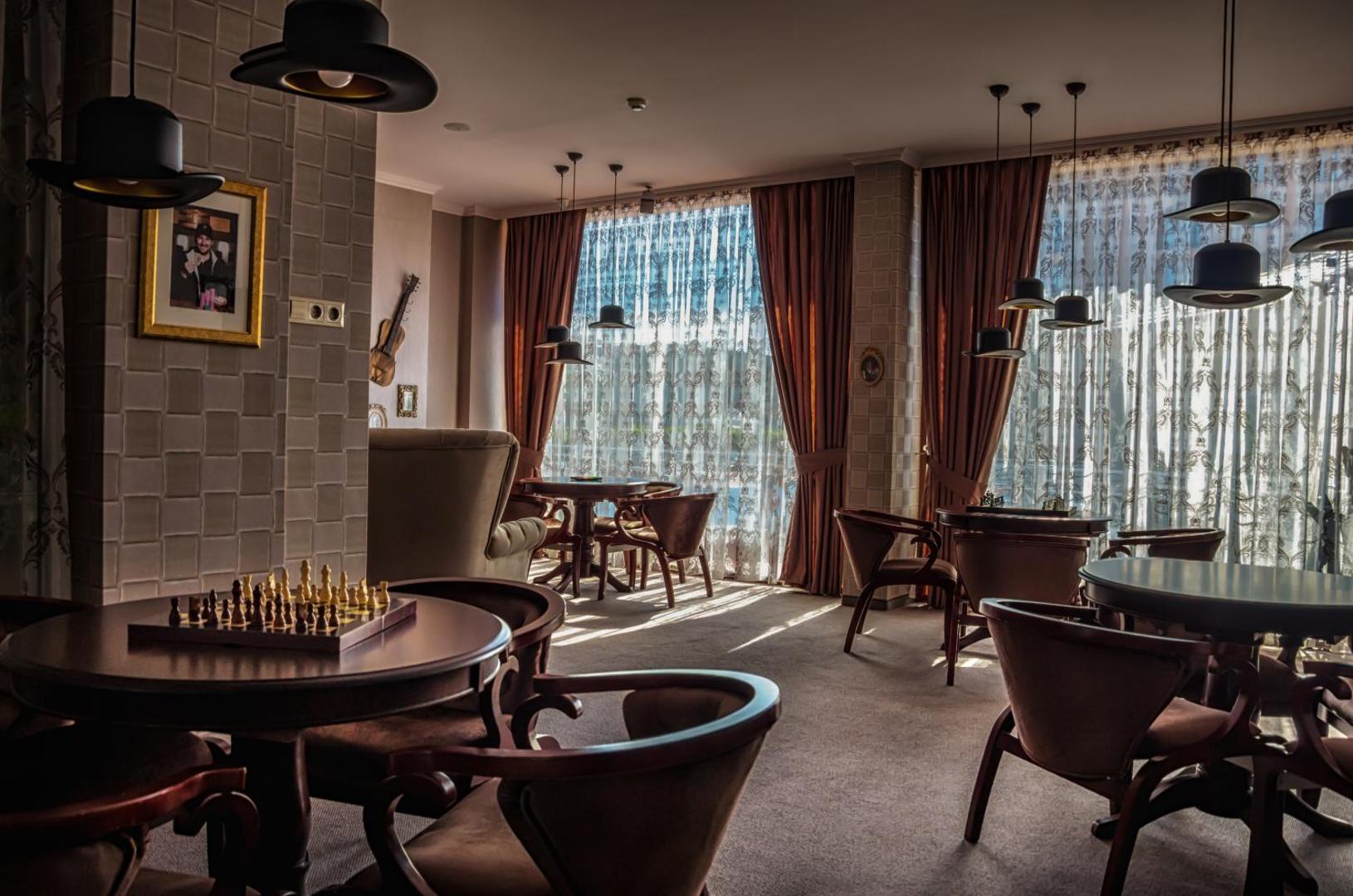 Diamant Residence Hotel & Spa atpūtas telpa ar šaha galdiem, klasiskām mēbelēm un oriģināliem gaismas ķermeņiem cepuru formā.