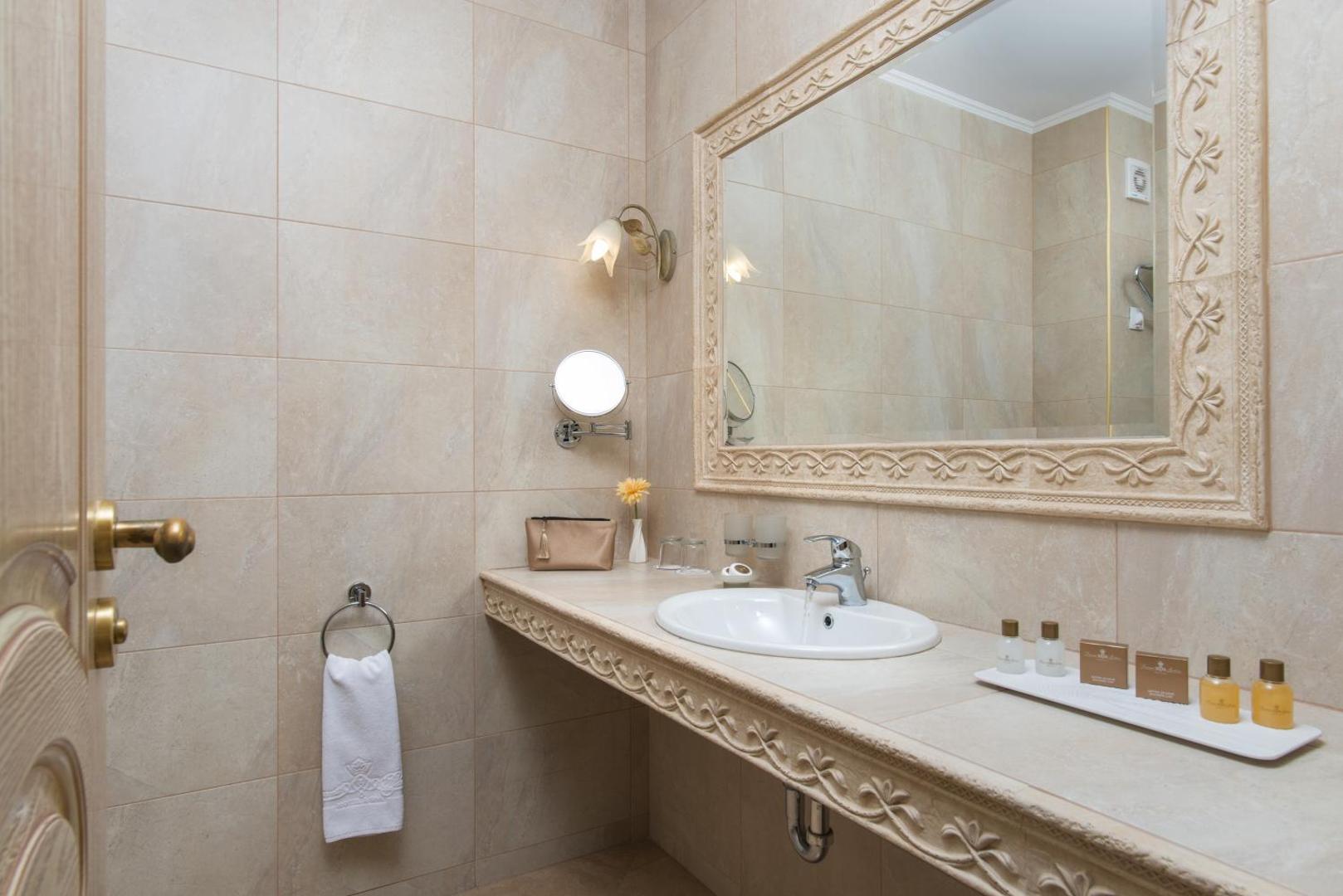 Diamant Residence Hotel & Spa numura vannas istaba ar gaišām flīzēm, lielu spoguli un higiēnas piederumu komplektu — klasisks dizains