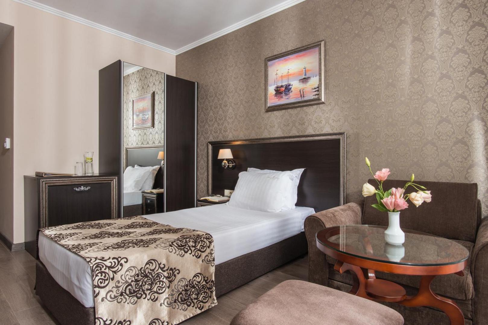 Diamant Residence Hotel & Spa gaišs viena cilvēka numurs ar tumša koka mēbelēm, spoguli un atpūtas zonu ar dīvānu.