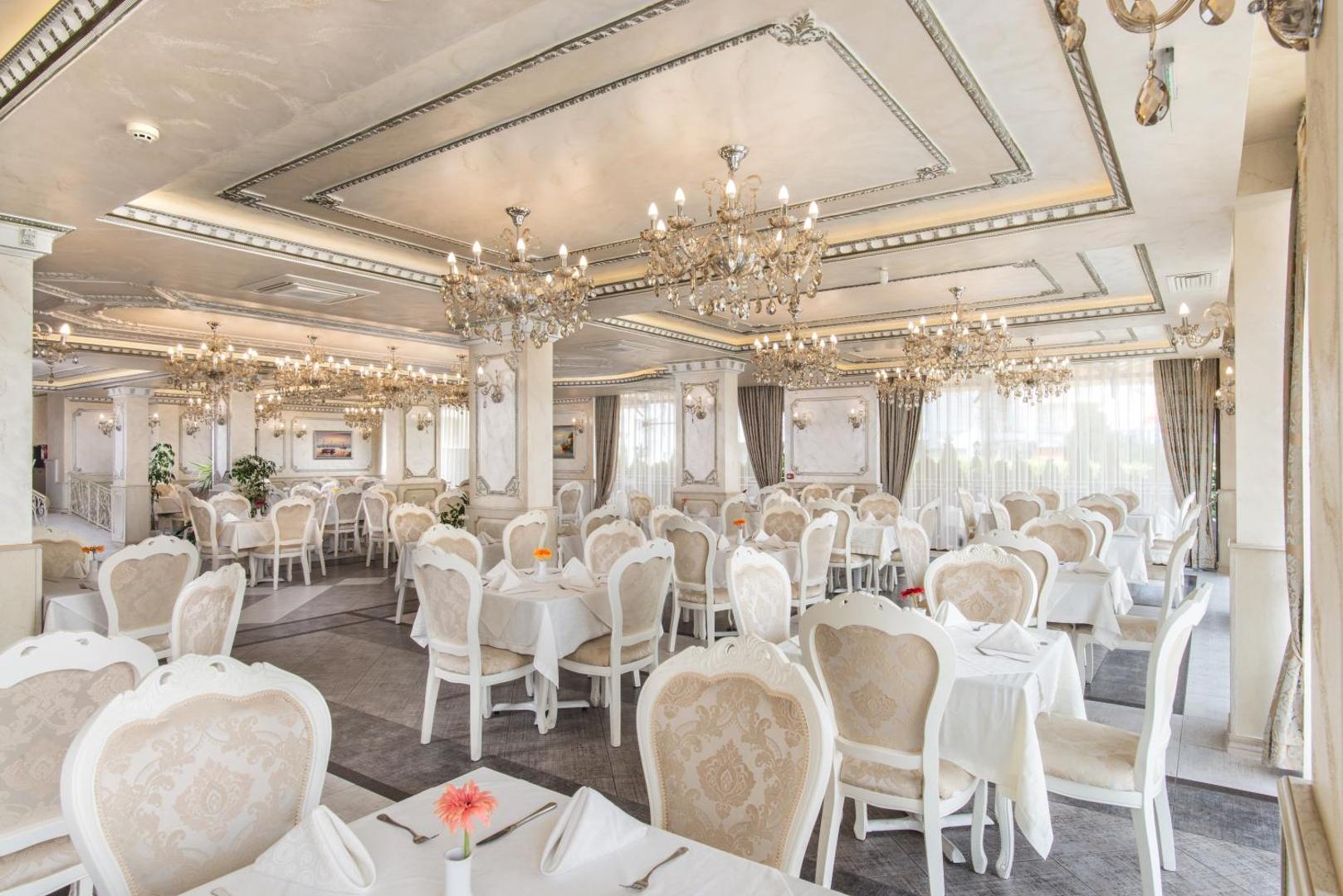 Diamant Residence Hotel & Spa elegantais restorāns ar baltiem krēsliem, kristāla lustrām un klasisku interjeru svinīgām vakariņām