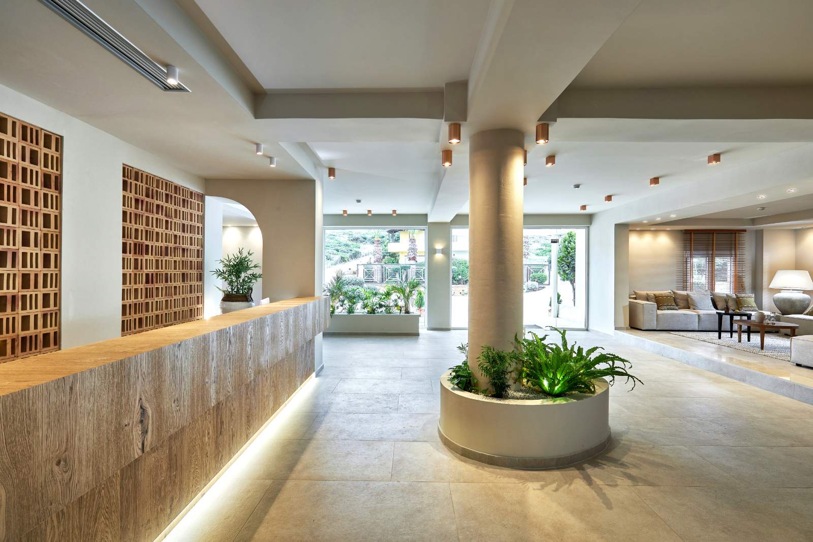 Vasia Hotel & Spa modernā recepcijas zona Krētā ar koka apdares leti, gaišām flīzēm un dekoratīviem augiem foajē centrā