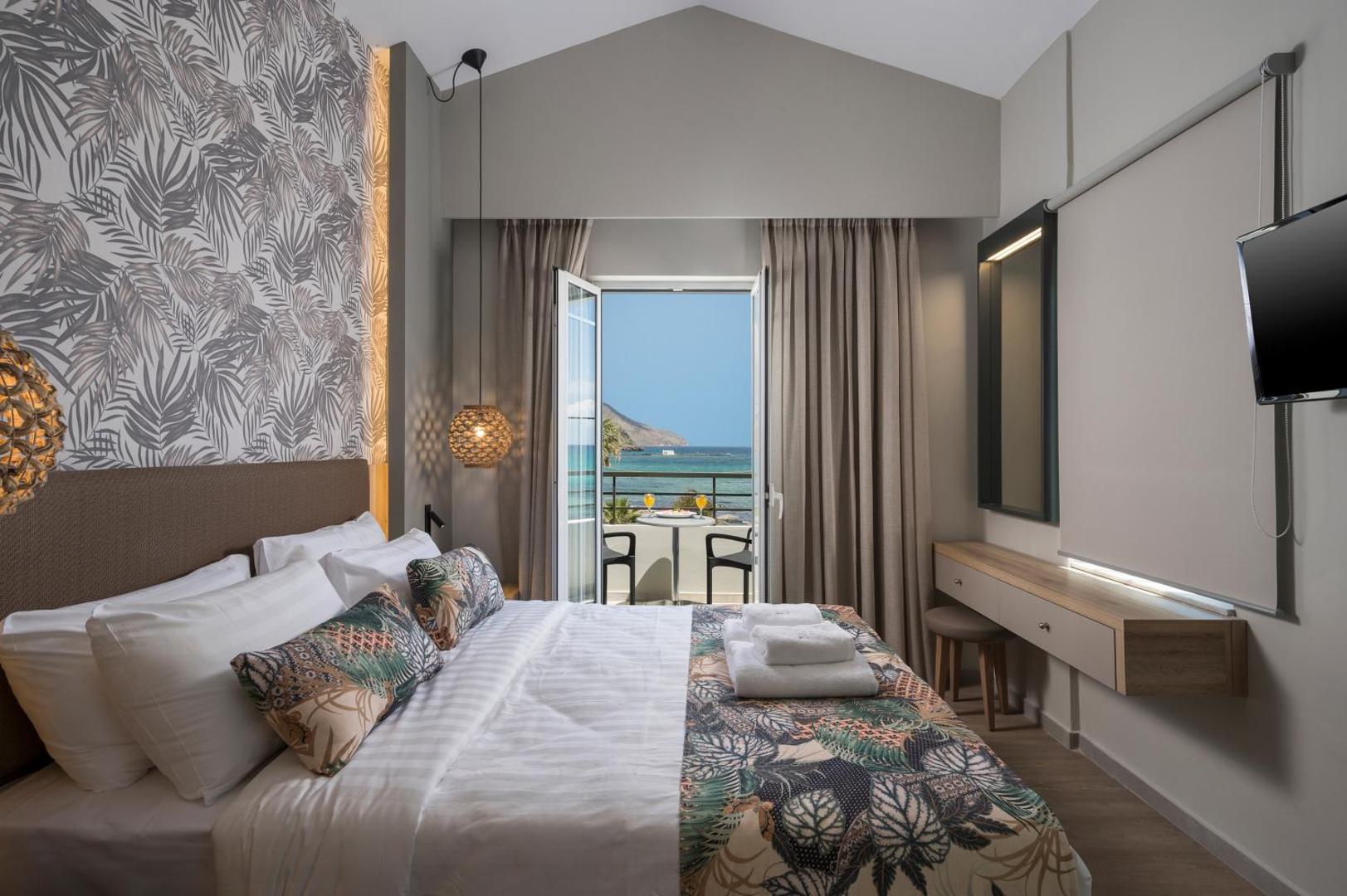 Mare Blue Suites gaišs numurs ar divguļamo gultu, modernu interjeru un balkonu, no kura redzama jūra
