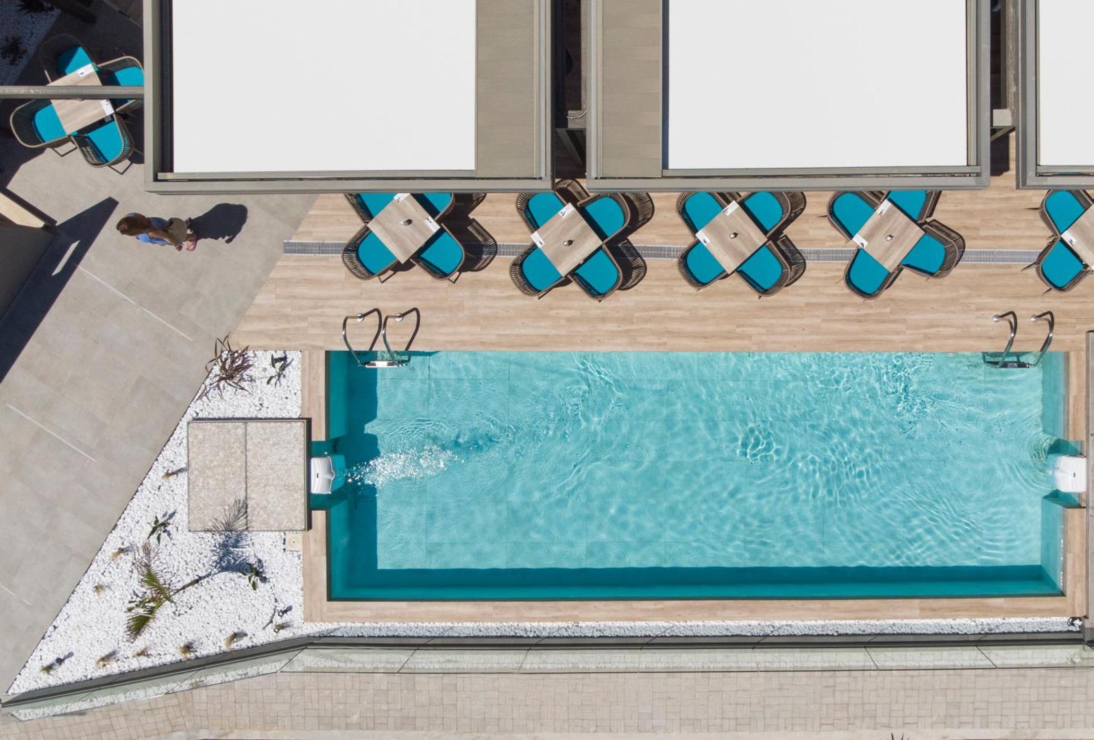Mare Blue Suites skats no augšas uz baseinu un atpūtas zonu ar stilīgiem galdiņiem un tirkīza krēsliem