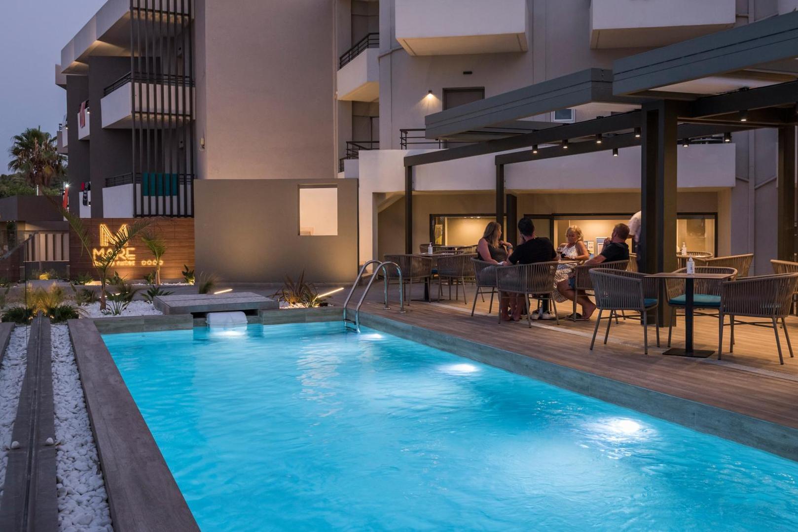 Mare Blue Suites āra baseins vakarā ar apgaismojumu un blakus esošo bāra zonu, kur atpūšas viesi