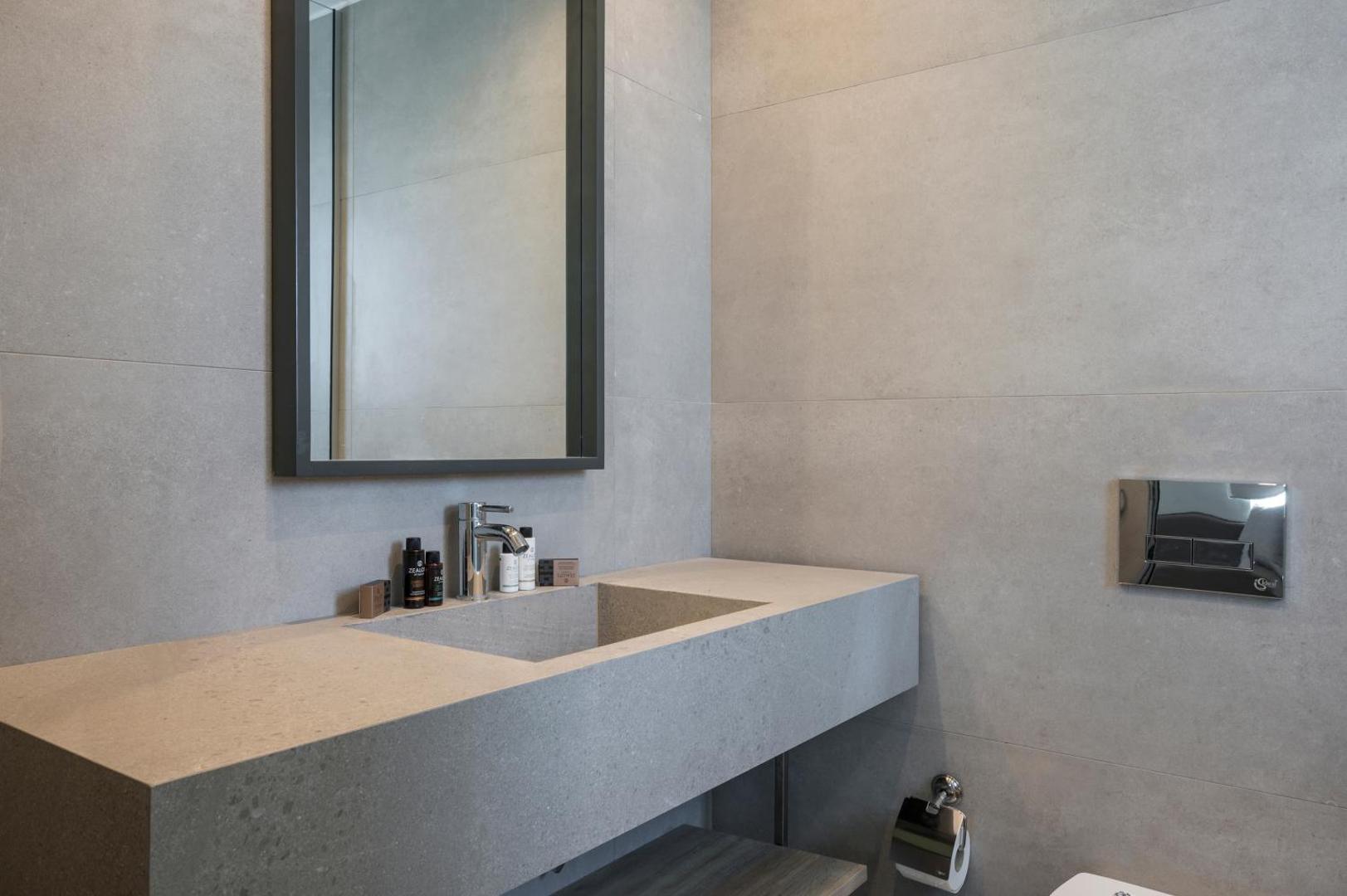 Mare Blue Suites numura vannas istabas interjers ar pelēkām akmens flīzēm, minimalistisku izlietni un lielu spoguli