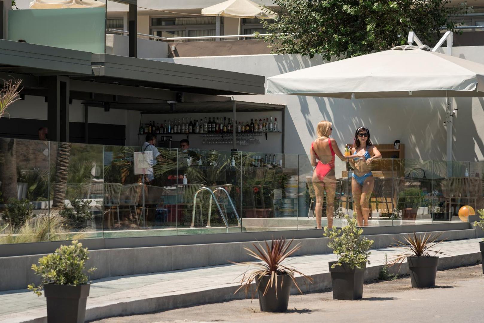Mare Blue Suites bāra zona pie baseina dienas laikā — viesi bauda kokteiļus pie stikla nožogojuma saulainā laikā Krētas kūrortā