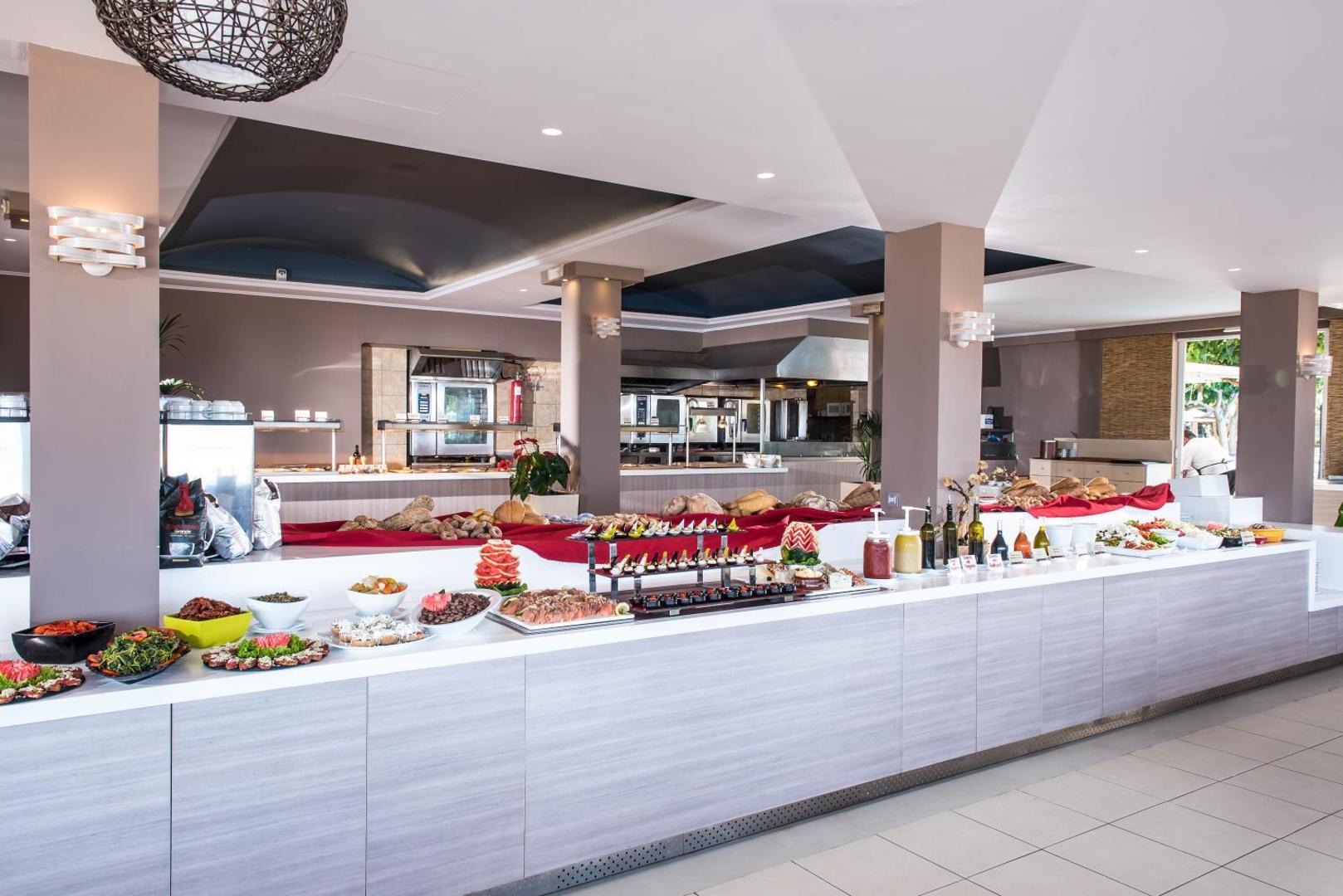 Corissia Beach Hotel bufetes tipa restorāna interjers ar plašu uzkodu un desertu izvēli — gaiša un moderna ēdamzāle