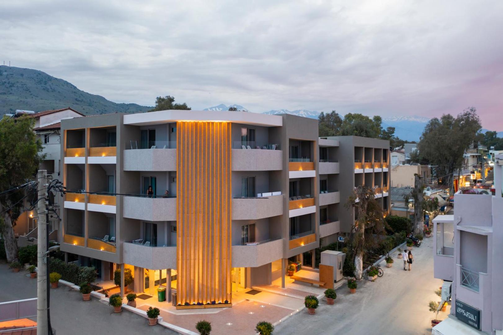 Corissia Beach Hotel ēkas izgaismotā fasāde vakara stundā Georgiupoli, Krētā — silts apgaismojums uz balkoniem un pie ieejas.