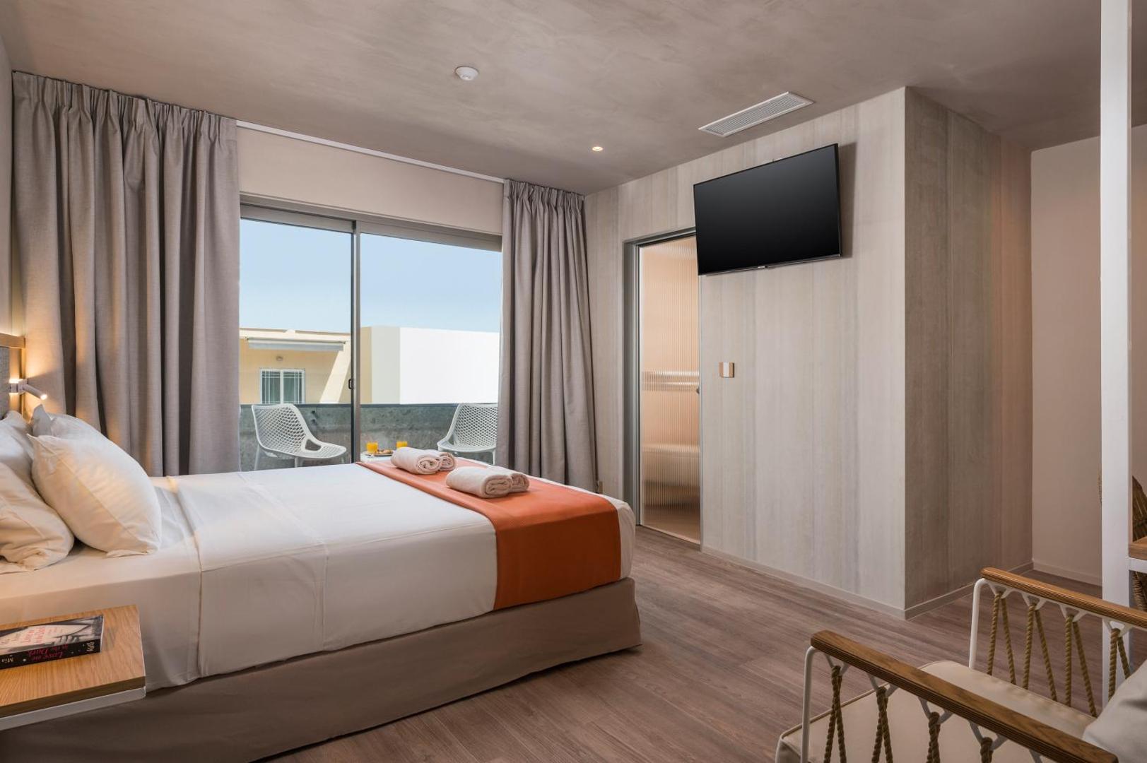 Corissia Beach Hotel numura skats uz balkonu un vannasistabas ieeju, moderns apgaismojums un koka grīdas segums.