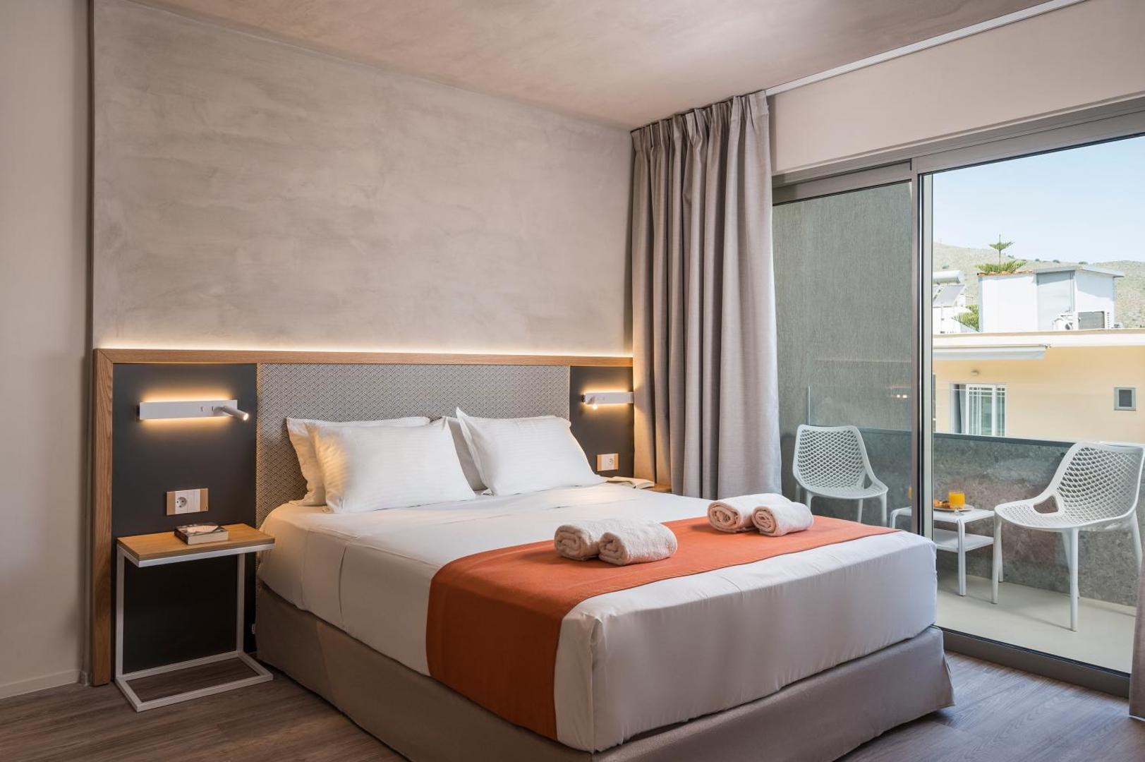 Corissia Beach Hotel moderns divvietīgs numurs ar balkonu, gaišu interjeru un oranžiem akcentiem Georgiupoles kūrortā, Krētas salā.