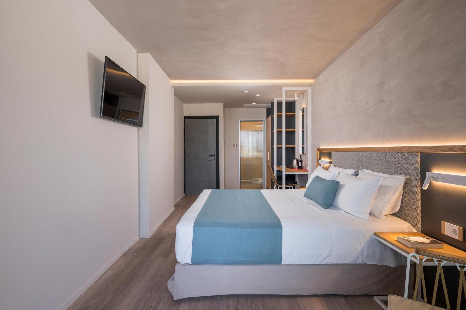 Corissia Beach Hotel numura interjers ar sienas televizoru, darba zonu un ērtu gultu gaišos toņos Georgiupoles kūrortā.