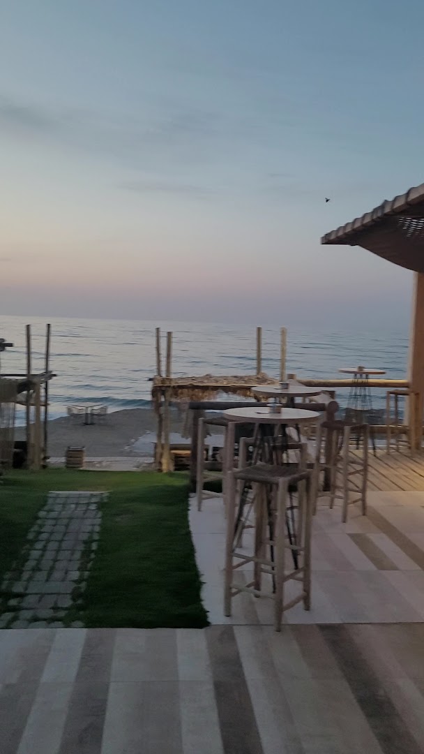 La Mer Resort & Spa āra terase ar augstajiem galdiem un krēsliem pie jūras saulrietā Krētā
