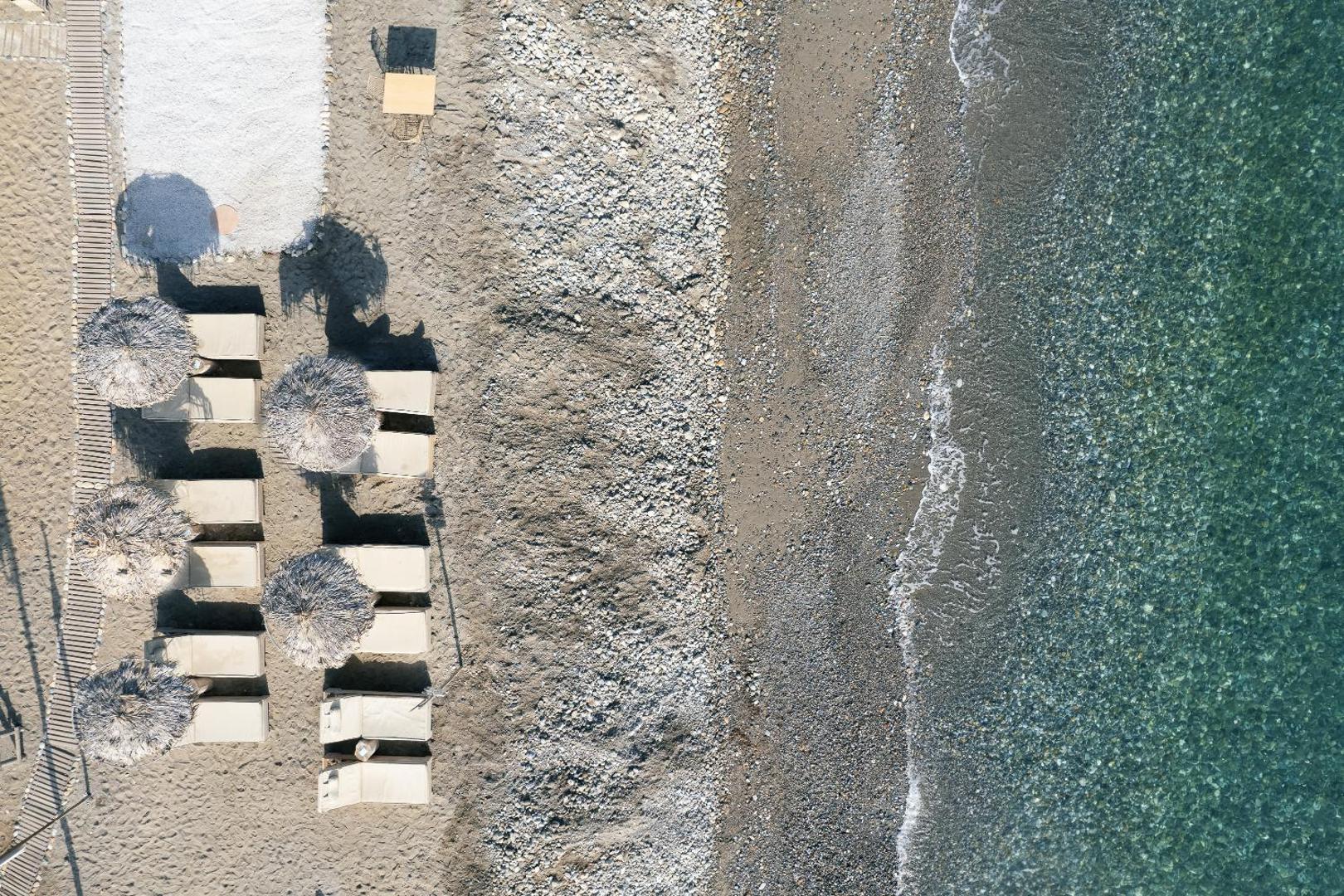 La Mer Resort & Spa privātā pludmale Krētā no putna lidojuma — saulessargi un zviļņi pie dzidra, tirkīzzila jūras ūdens