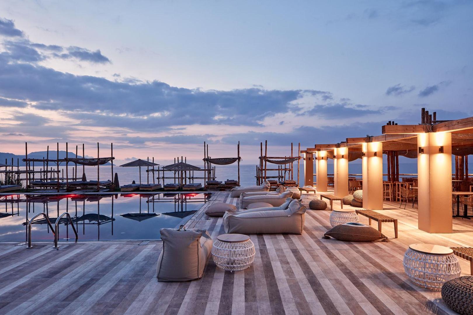 La Mer Resort & Spa āra terase krēslas stundā ar mīkstajiem zviļņiem pie baseina un skatu uz jūru Georgiupoli reģionā, Krētā.