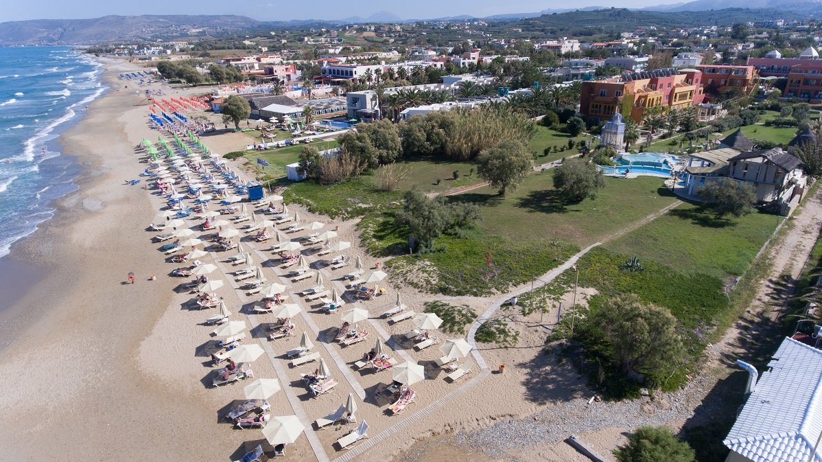 Orpheas Resort Hotel skats no putna lidojuma uz plašo smilšu pludmali, dārzu un viesnīcas korpusiem Georgiupoles piekrastē, Krētā