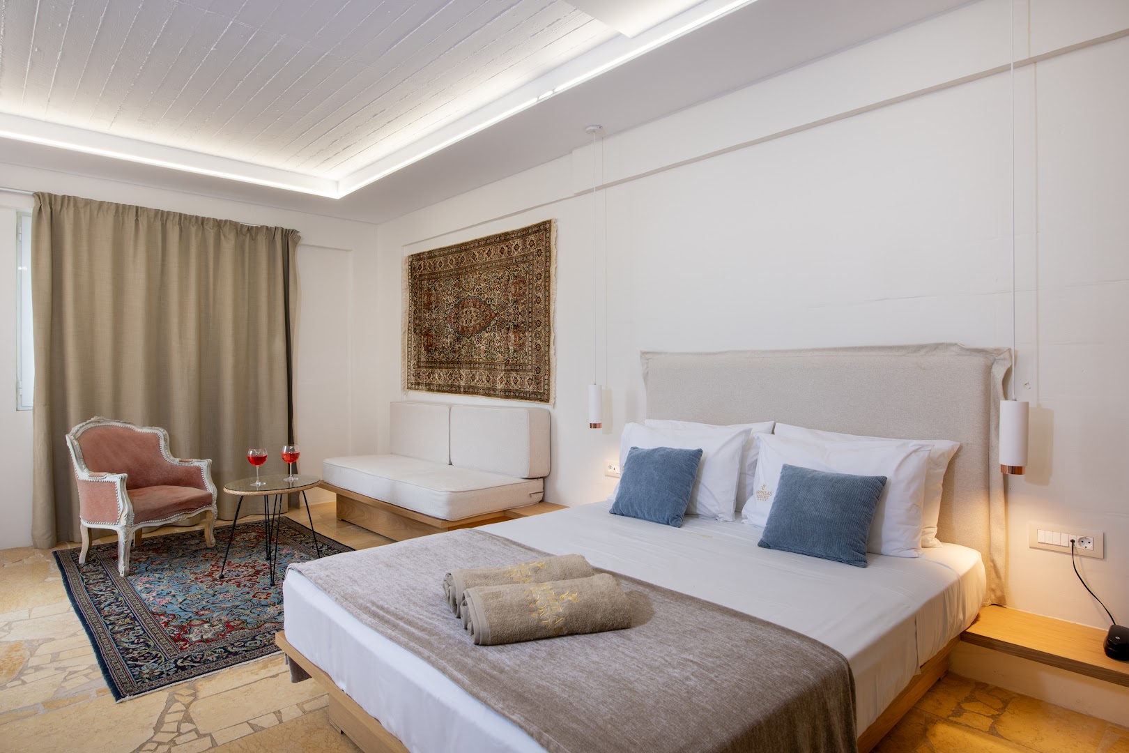 Orpheas Resort Hotel numura interjers ar lielu gultu, dekoratīvu sienas paklāju un akmens flīžu grīdu Krētas kūrortā