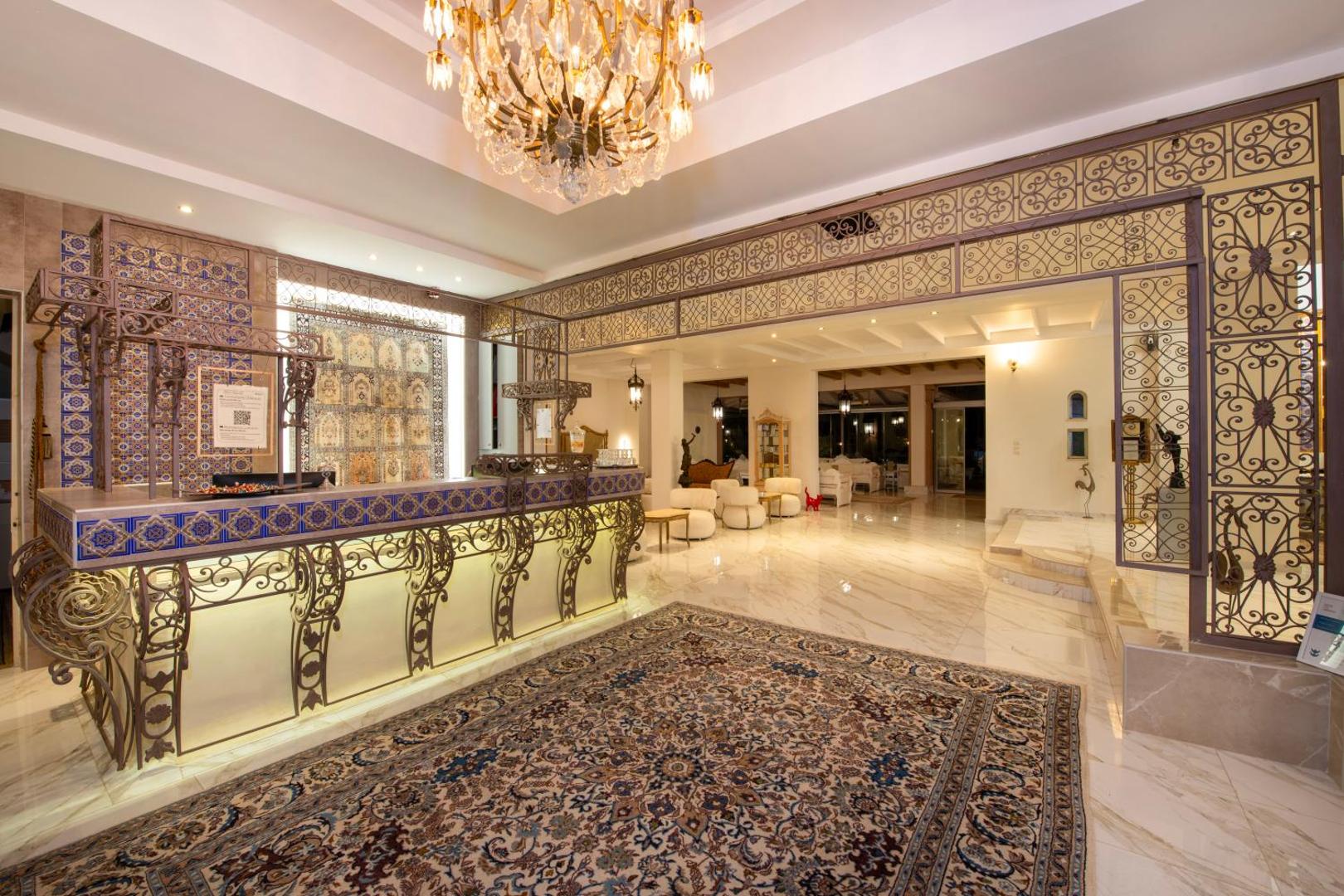 Orpheas Resort Hotel grezna recepcijas zona Georgiupoli, Krētā — dekoratīvi metāla elementi, kristāla lustra un austrumu stila paklāji gaišā foajē