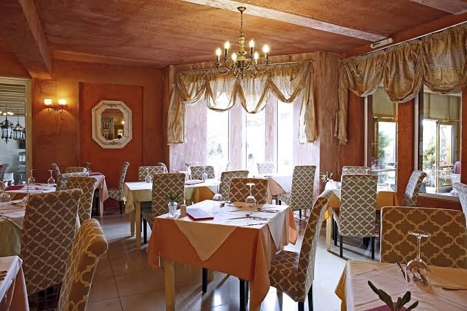 Orpheas Resort Hotel restorāna zāle ar eleganti klātiem galdiem, klasiskām lustrām un lieliem logiem uz dārzu