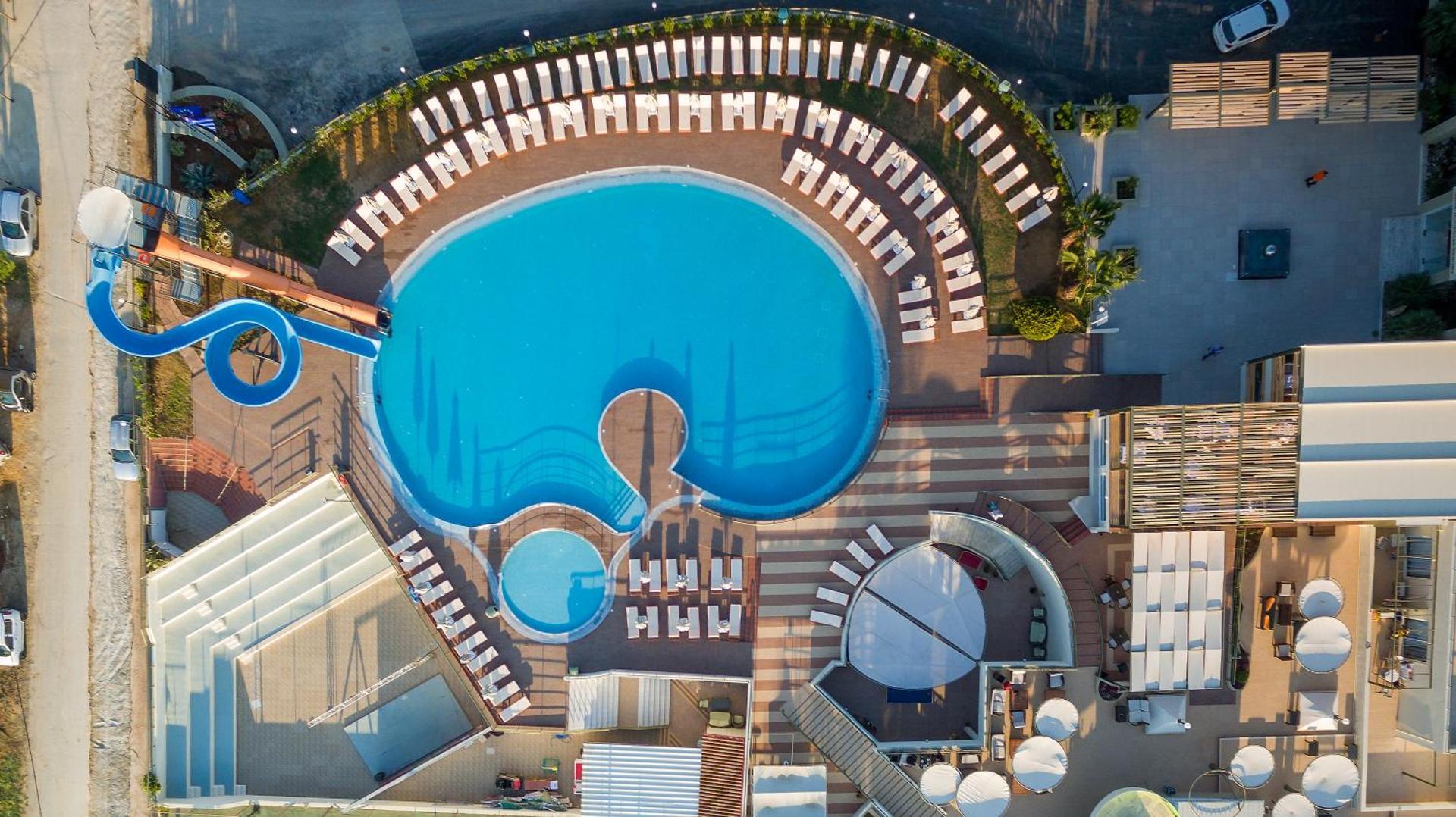 Aerofoto skats uz Georgioupolis Resort apaļo baseinu, sauļošanās terasi ar daudziem krēsliem un blakus esošo bērnu baseinu no putna lidojuma