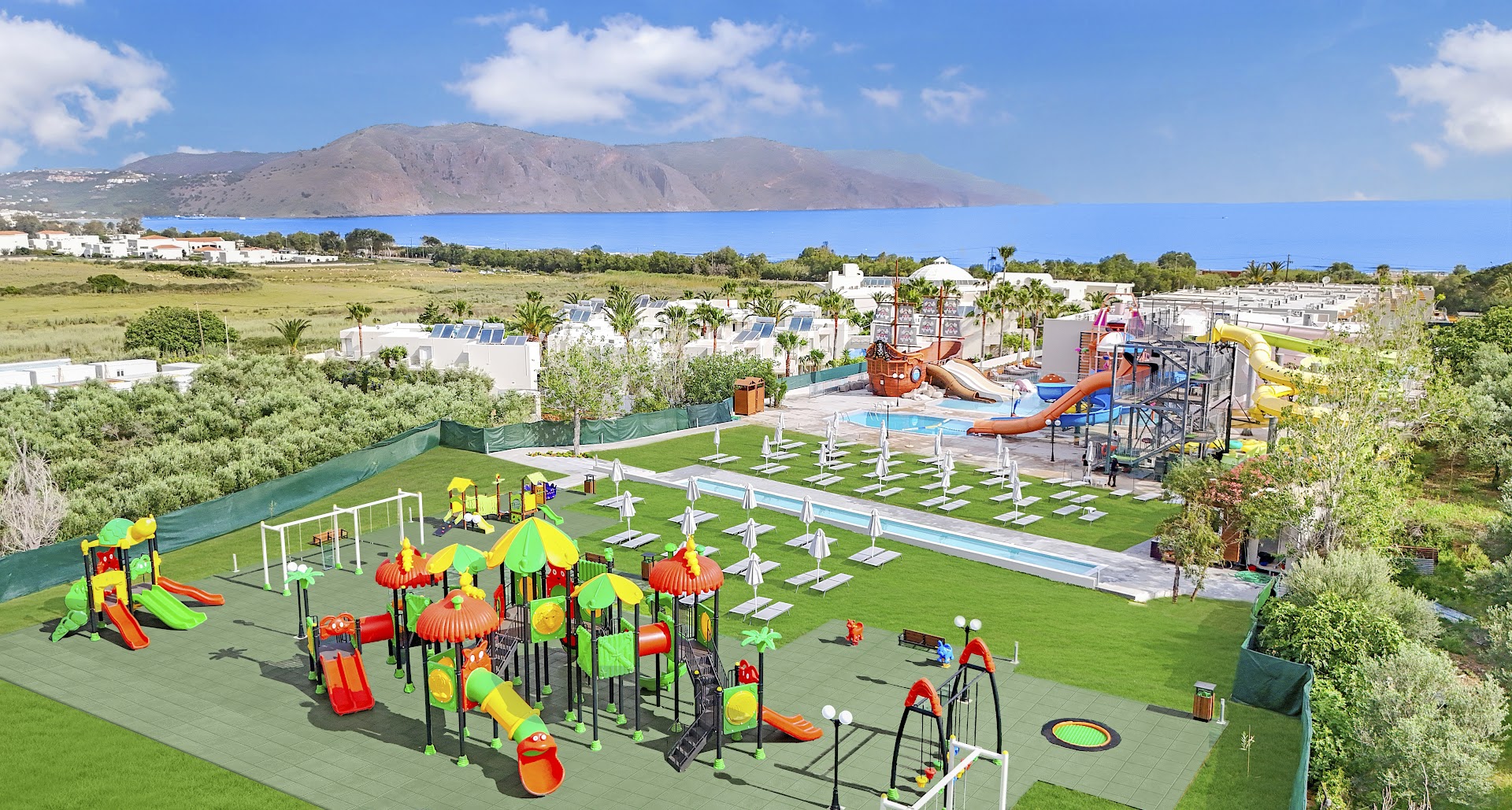Georgioupolis Resort Aqua Park panorāmas skats uz teritoriju, akvaparku un bērnu laukumu ar kalniem un jūru fonā