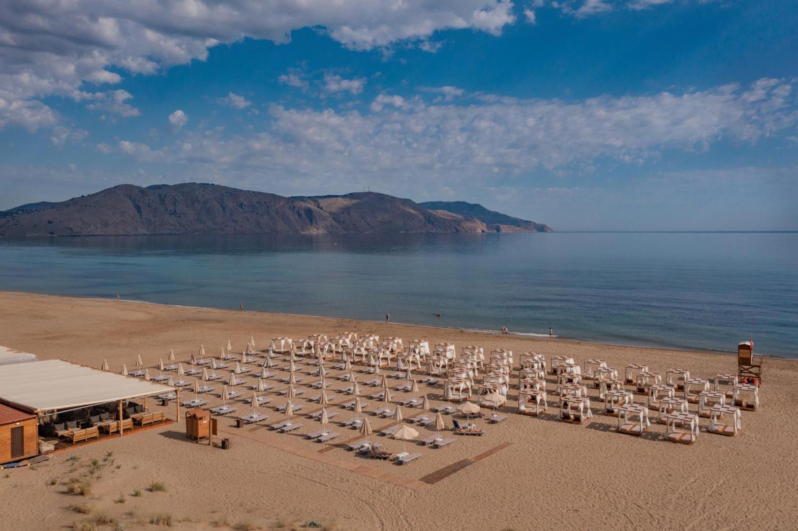 Georgioupolis Resort Aqua Park and SPA plašā smilšu pludmale ar saulessargiem un gultām pie zilās jūras