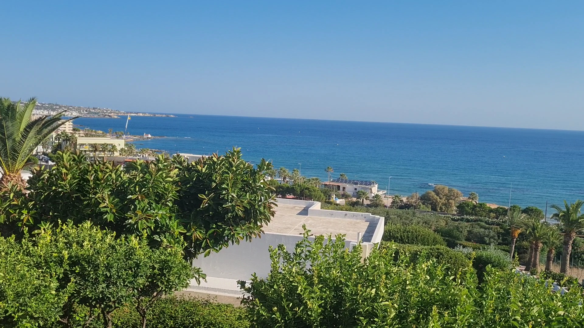 Skats no King Minos Retreat Resort & Spa uz Vidusjūras piekrasti un Hersonisas kūrortpilsētu caur zaļojošu dārzu