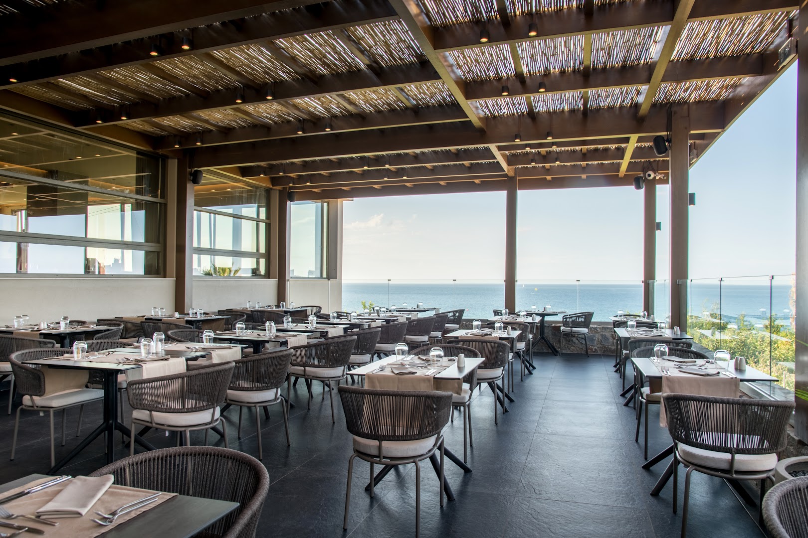 King Minos Retreat Resort & Spa restorāna āra terase ar skatu uz jūru Hersonisā, Krētā — eleganti galdiņi zem koka nojumes