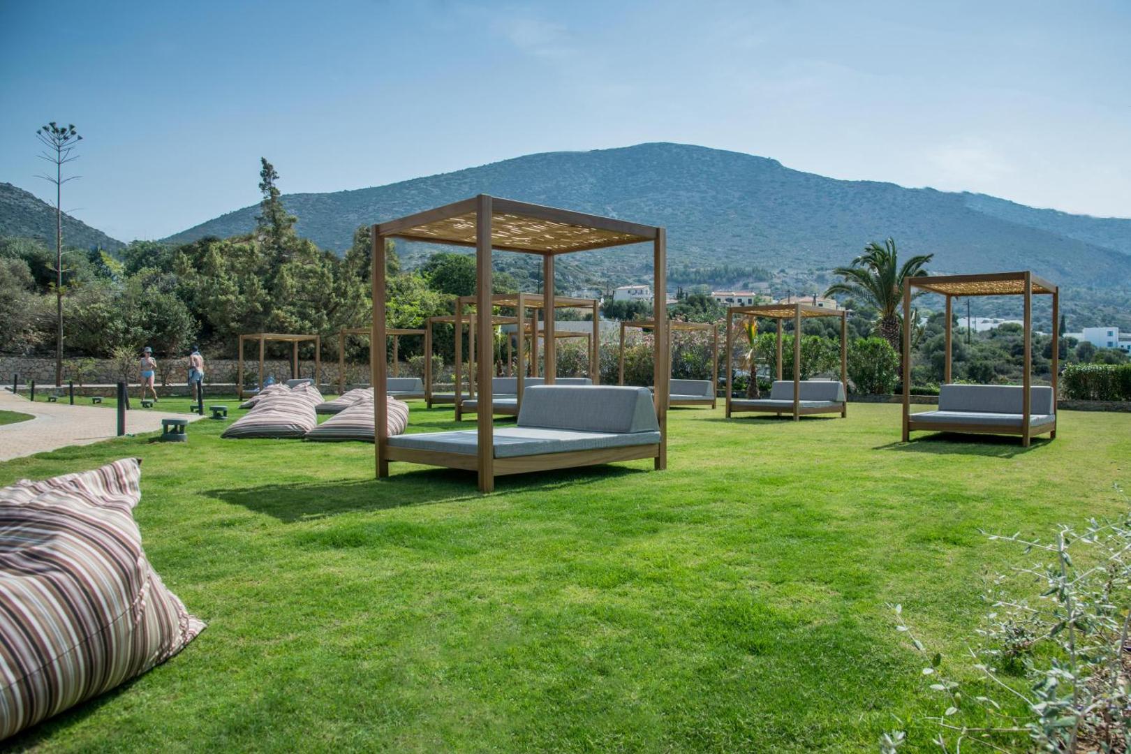 King Minos Retreat Resort & Spa atpūtas zona dārzā ar mīkstiem zviļņiem un nojumēm uz zaļa zālāja ar skatu uz kalniem