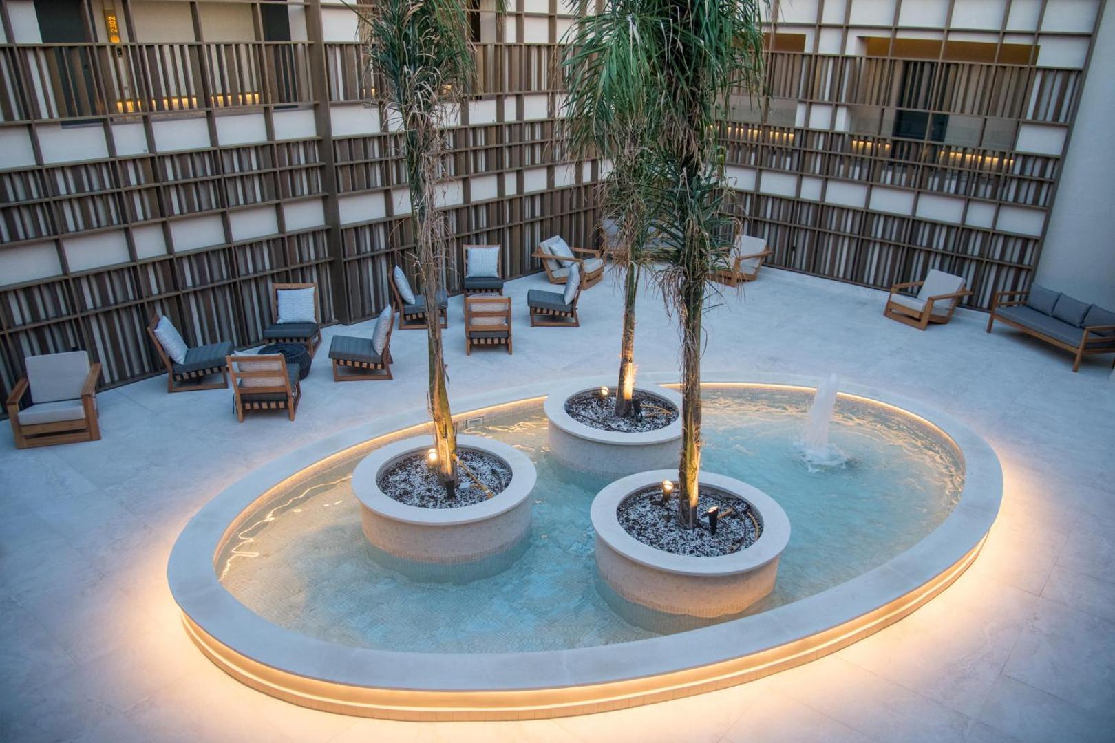 King Minos Retreat Resort & Spa iekšpagalms ar dekoratīvu baseinu, strūklaku un palmām, ko ieskauj atpūtas krēsli un moderna arhitektūra