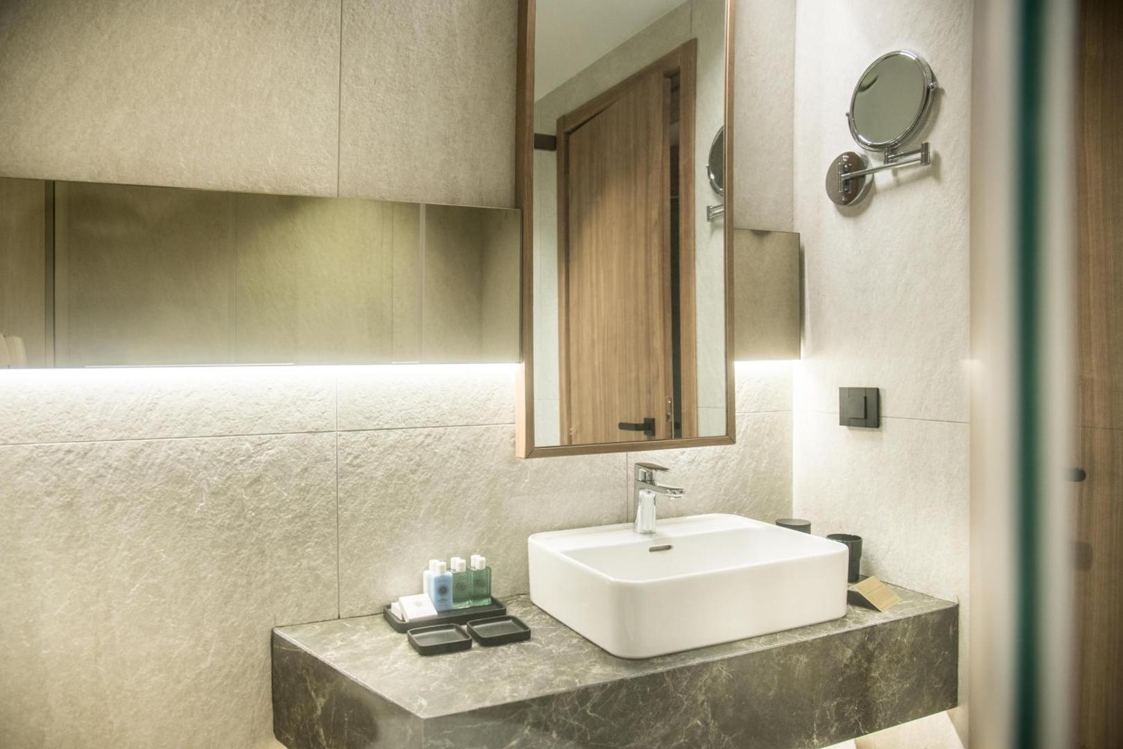 King Minos Retreat Resort & Spa moderna vannas istaba ar akmens apdari, baltu izlietni, lielu spoguli un higiēnas piederumiem