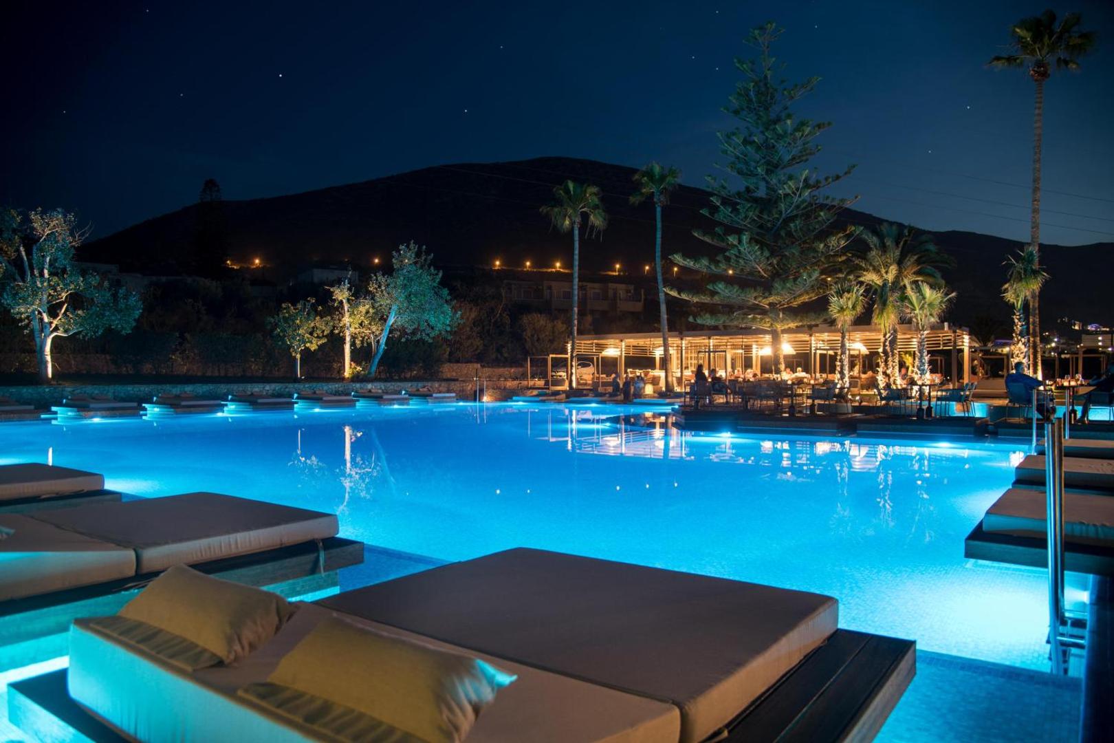 King Minos Retreat Resort & Spa baseina zona naktī ar izgaismotu ūdeni un restorāna terasi fonā Hersonisas reģionā