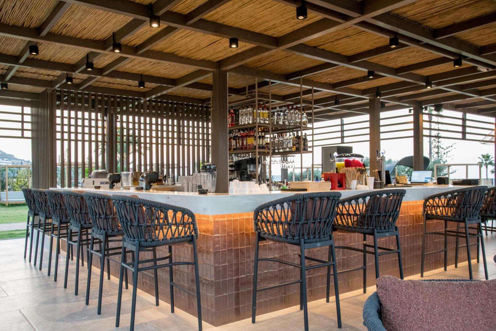 King Minos Retreat Resort & Spa āra bārs ar stilīgiem krēsliem un koka jumta konstrukciju Krētas piekrastē