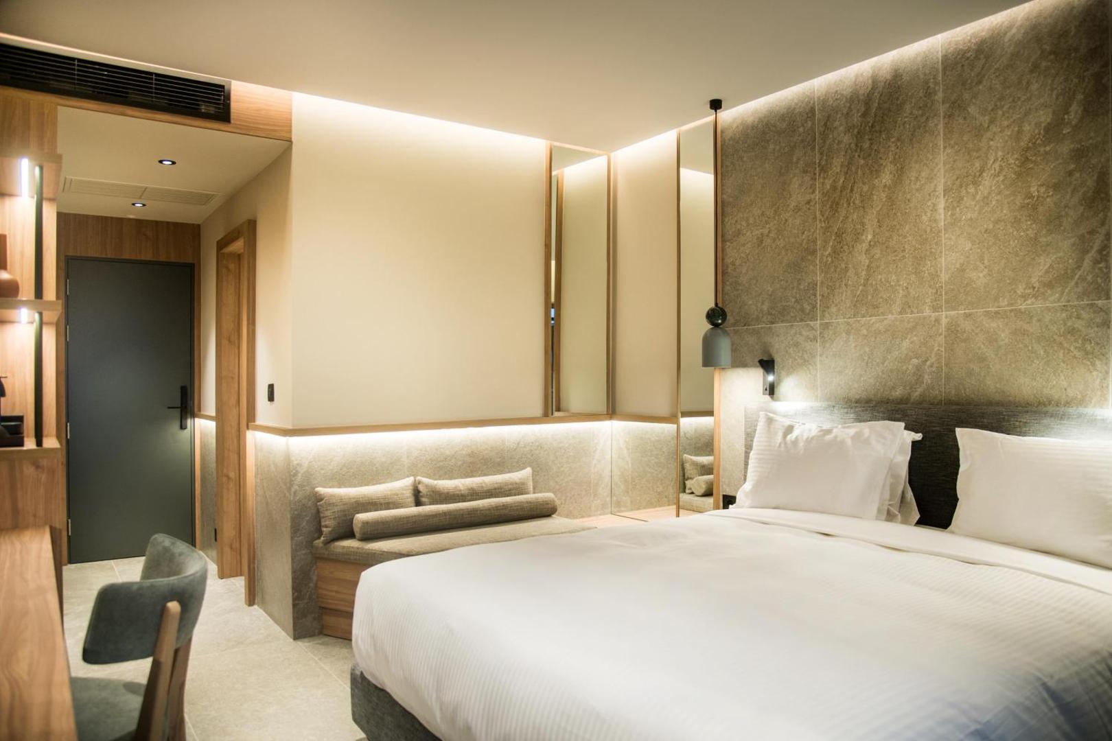 King Minos Retreat Resort & Spa moderns viesnīcas numurs ar gaišu interjeru, akmens sienas apdari un lielu divguļamo gultu