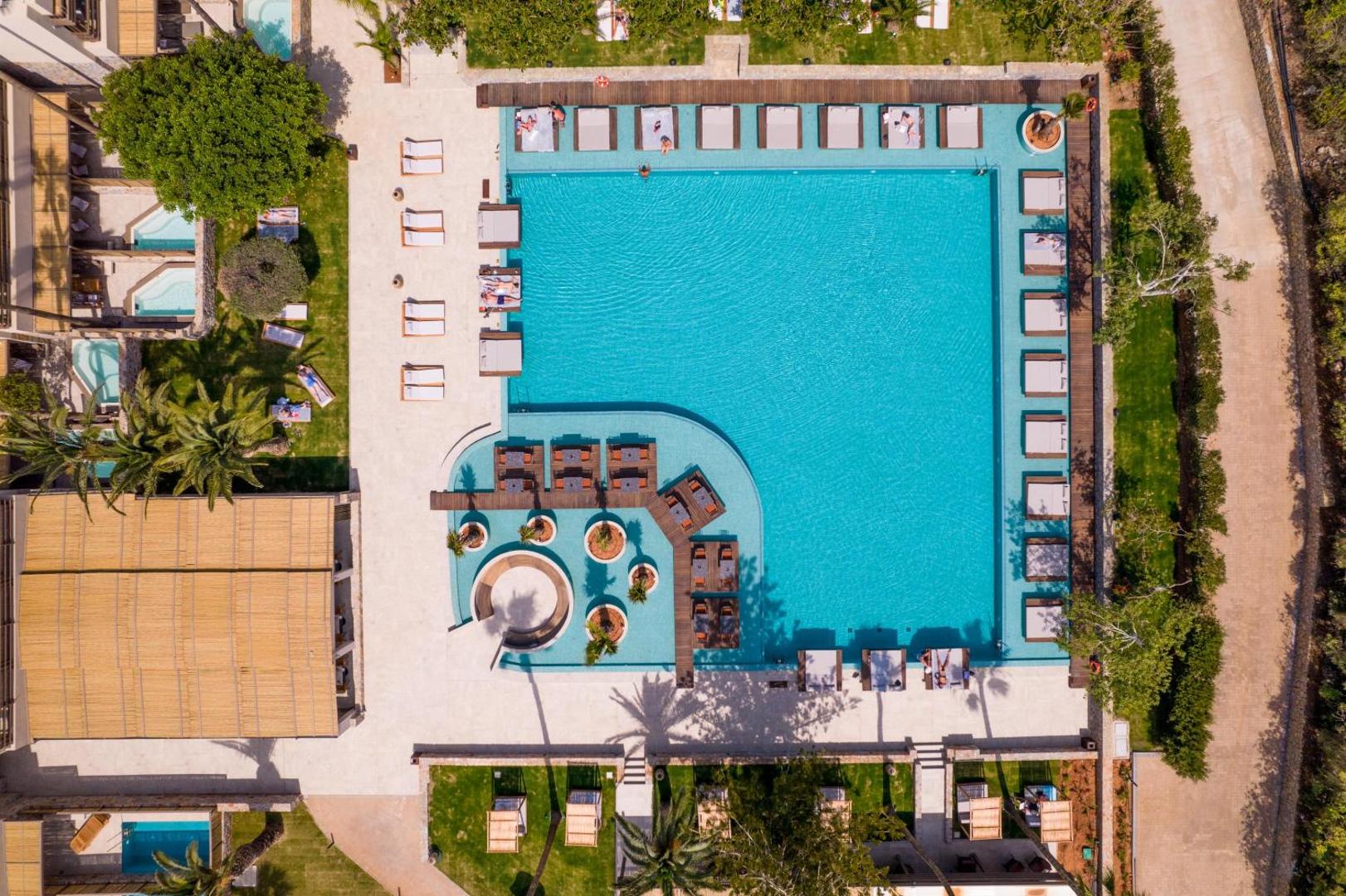 King Minos Retreat Resort & Spa galvenais baseins no putna lidojuma Hersonisā, Krētā — plaša atpūtas zona ar sauļošanās gultām un palmām