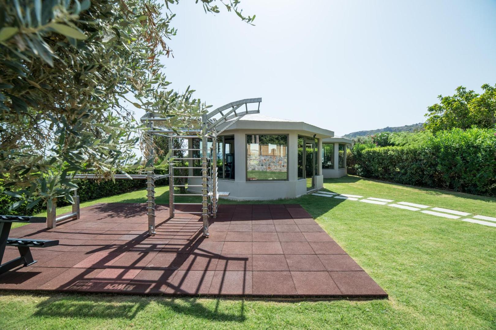 King Minos Retreat Resort & Spa āra trenažieru zona un fitnesa paviljons Krētā — sporta aprīkojums uz speciāla seguma zaļā dārzā