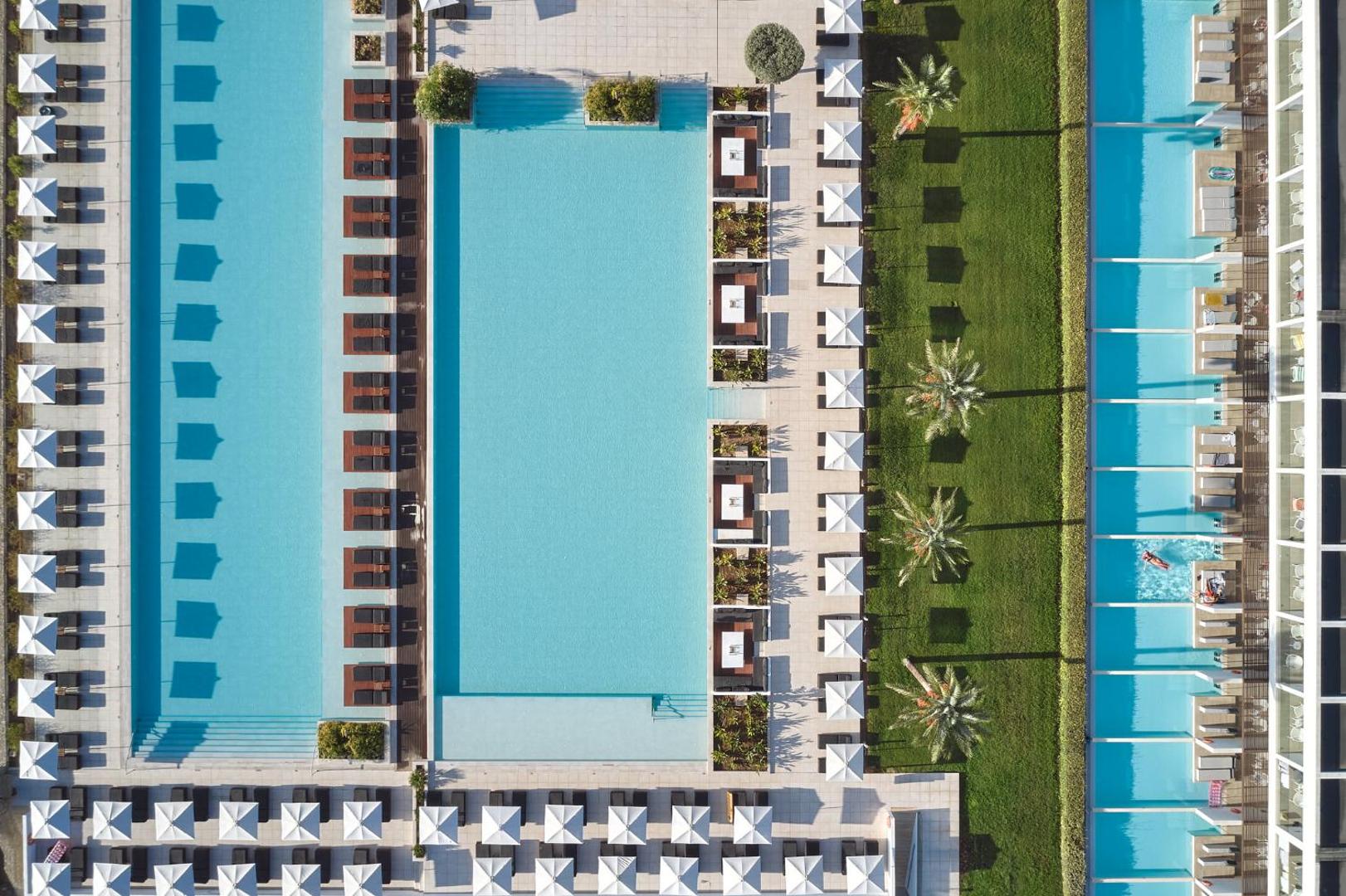 Gennadi Grand Resort teritorijas skats no putna lidojuma ar vairākiem baseiniem, zaļo zonu, palmām un saulessargiem Rodā