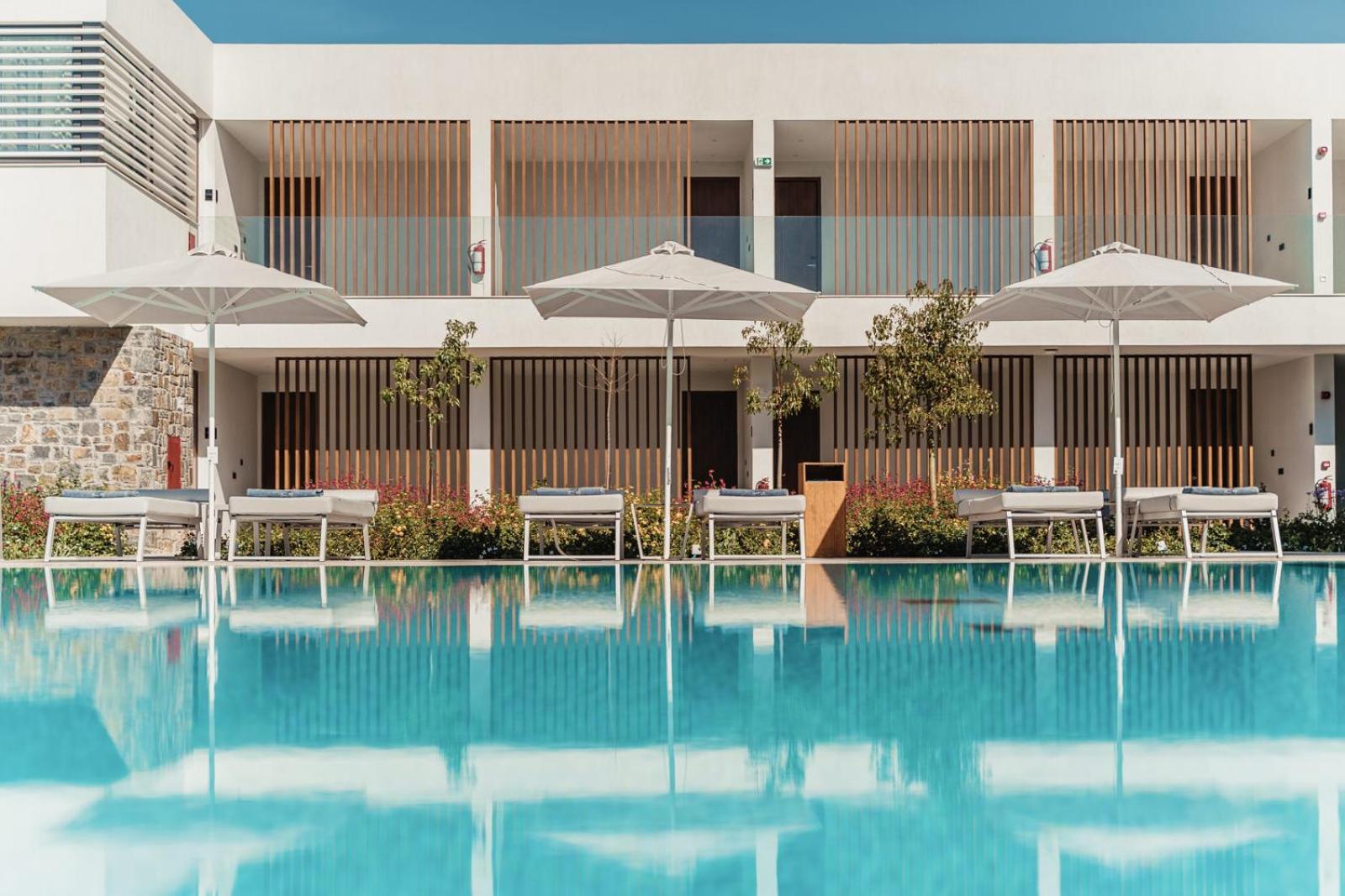 Gennadi Grand Resort moderna viesnīcas ēka ar numuriem un baseinu priekšplānā Rodā — gaiša arhitektūra ar koka elementiem un saulessargiem