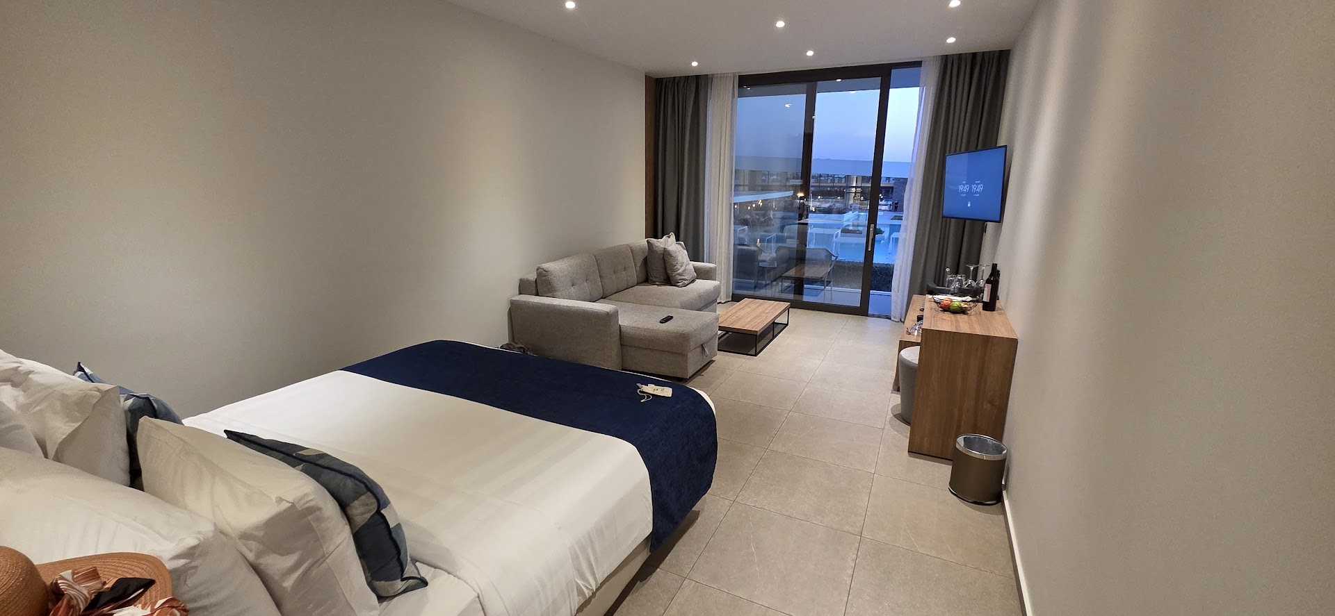 Gennadi Grand Resort mūsdienīgs viesnīcas numurs ar divguļamo gultu, dīvānu un skatu uz baseinu caur lieliem panorāmas logiem Rodas salā