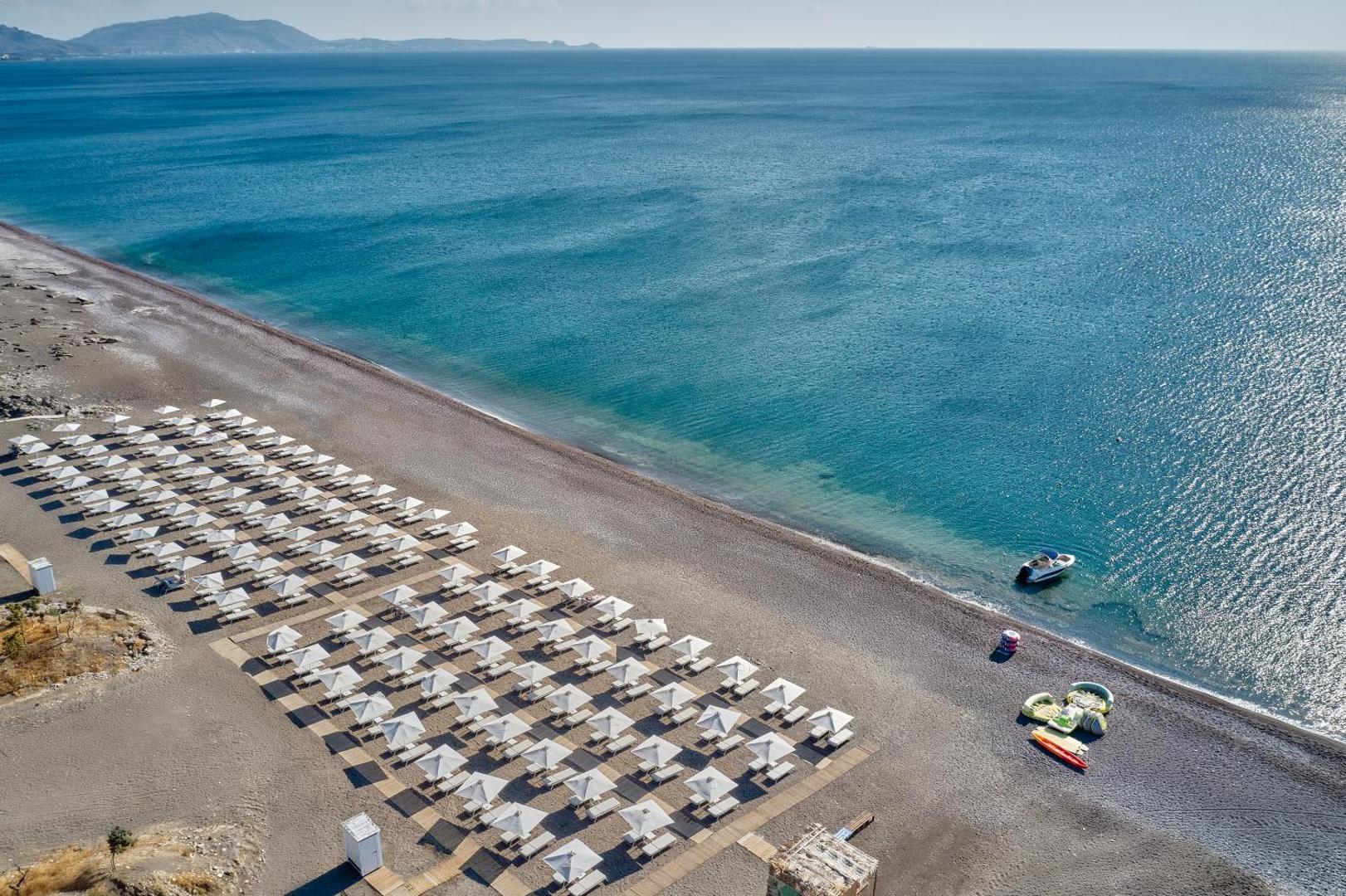 Gennadi Grand Resort plašā piekrastes zona ar saulessargiem un laivu ūdenī — panorāmas skats uz Rodas piekrasti
