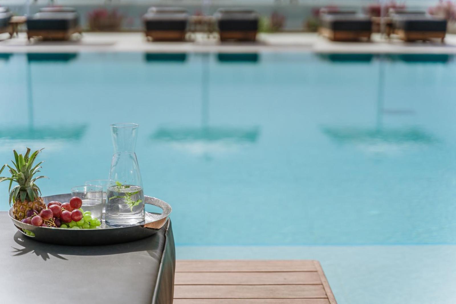 Gennadi Grand Resort āra baseins Rodas salā ar augļu paplāti un ūdens krūzi priekšplānā — relaksējoša atpūtas zona pie ūdens