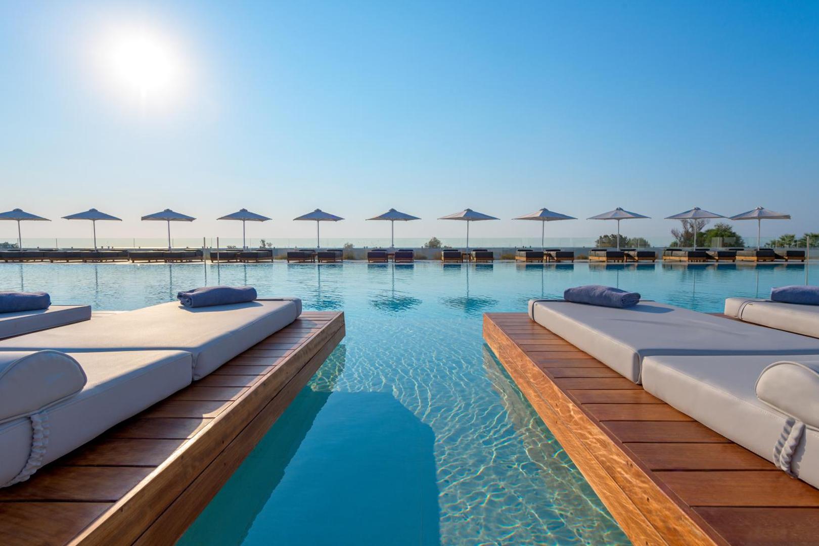 Gennadi Grand Resort āra baseins ar koka platformām un sauļošanās gultām Rodas salā, Grieķijā — skats uz horizontu saulainā dienā