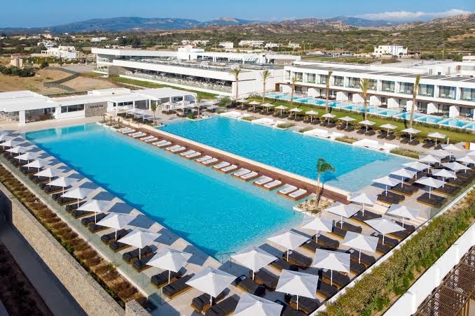 Gennadi Grand Resort modernā baseinu zona ar daudziem saulessargiem un atpūtas krēsliem, fonā redzami numuri ar piekļuvi baseinam