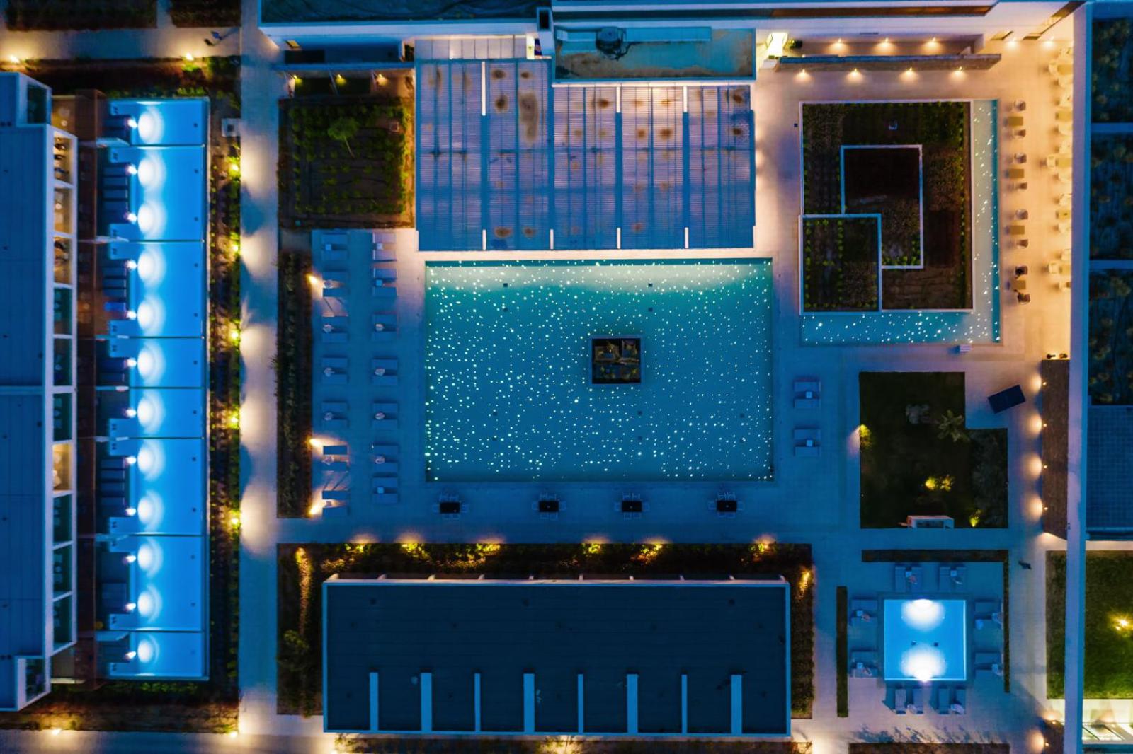 Gennadi Grand Resort viesnīcas teritorija vakarā no augšas ar izgaismotiem baseiniem un modernu arhitektūras apgaismojumu