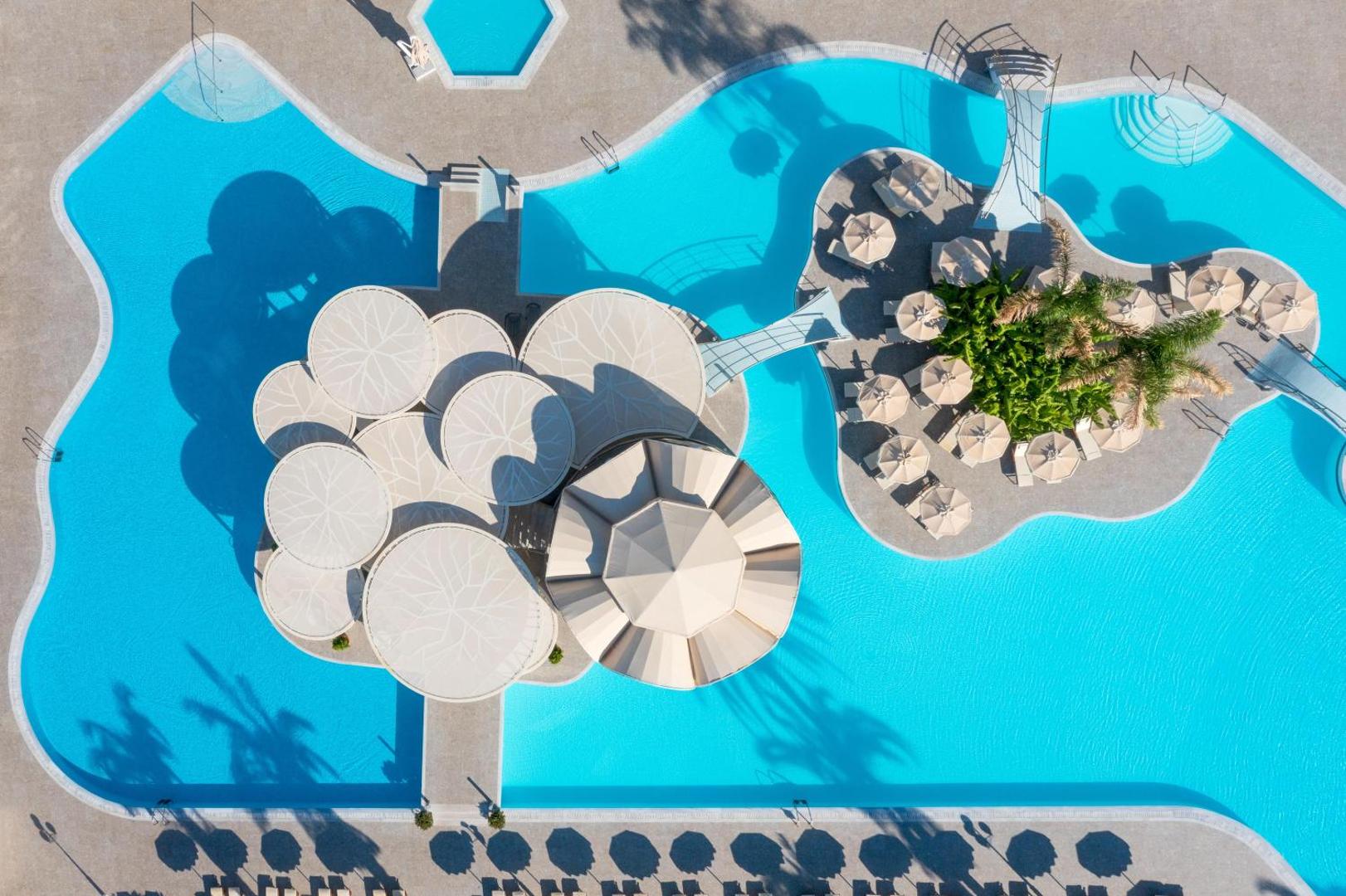 Rodos Palladium Leisure & Wellness viesnīcas galvenais baseins no putna lidojuma Rodas salā — redzama unikāla baseina bāra arhitektūra un atpūtas zonas