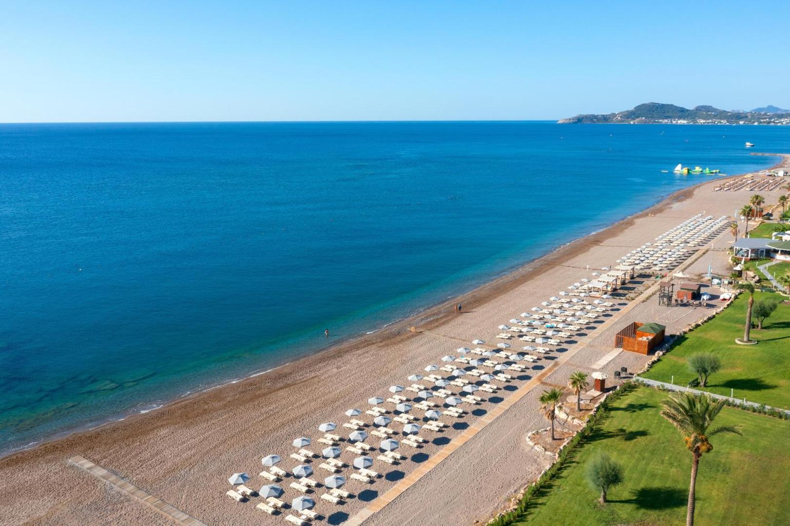 Aerofoto skats uz Rodos Palladium Leisure & Wellness privāto pludmali Faliraki, Rodā — zila jūra, smilšu krasts un saulessargi