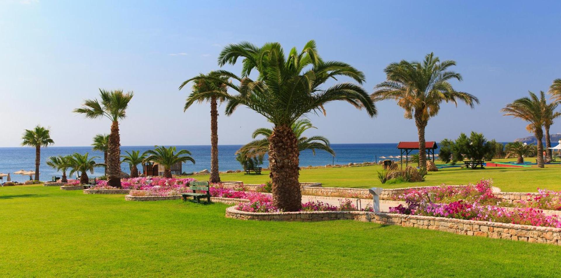 Rodos Palladium Leisure & Wellness viesnīcas dārzs ar palmām un ziedošām puķu dobēm Rodas salā, Grieķijā — skats uz Vidusjūru