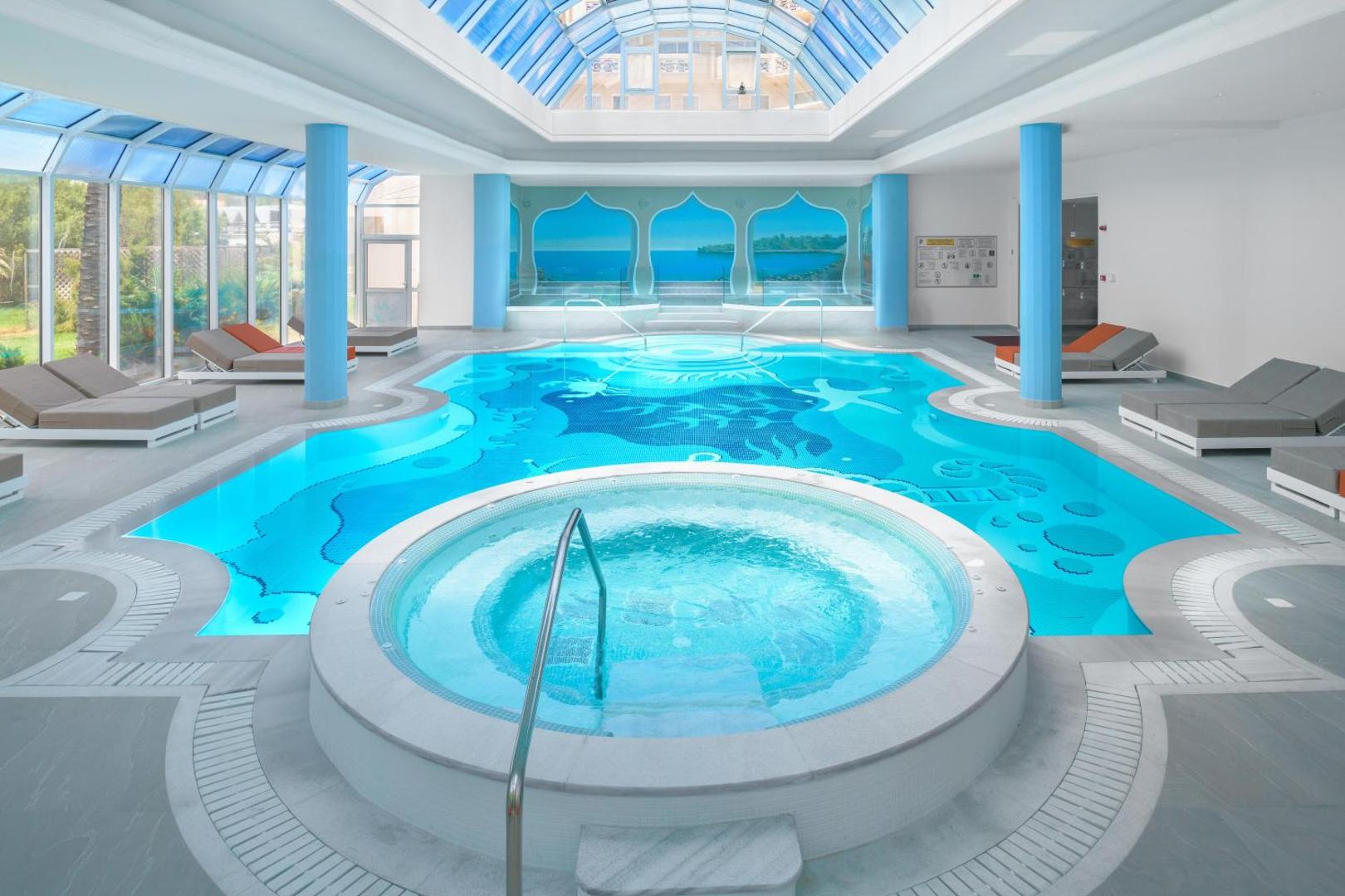 Rodos Palladium Leisure & Wellness iekštelpu spa baseins ar džakuzi un stikla jumtu — gaiša relaksācijas zona ar atpūtas krēsliem